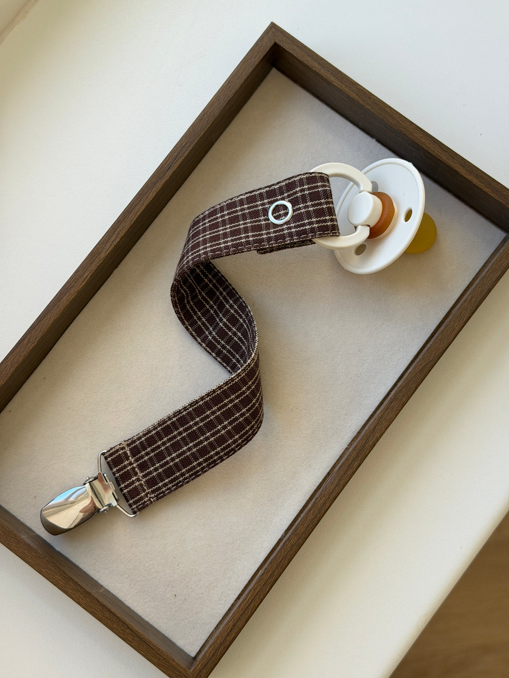 Close-up of Pecan dummy clip in reddish-brown check with a dummy in a wooden tray