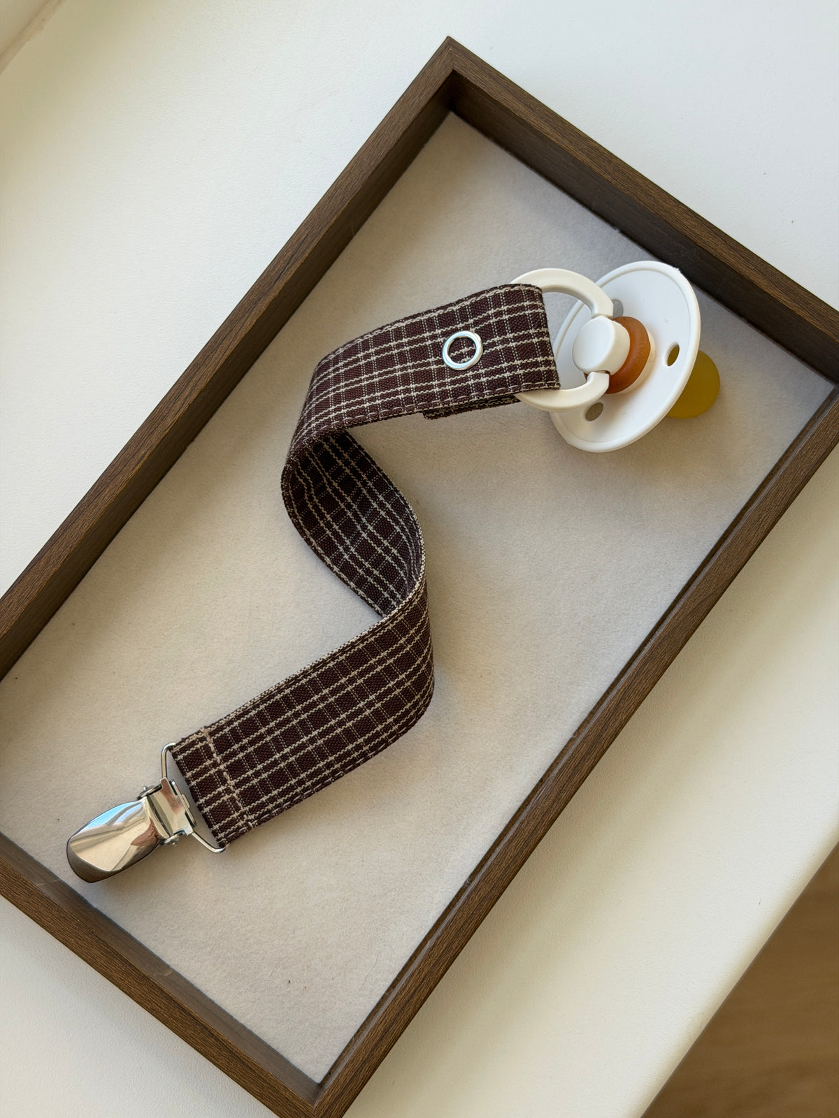 Close-up of Pecan dummy clip in reddish-brown check with a dummy in a wooden tray