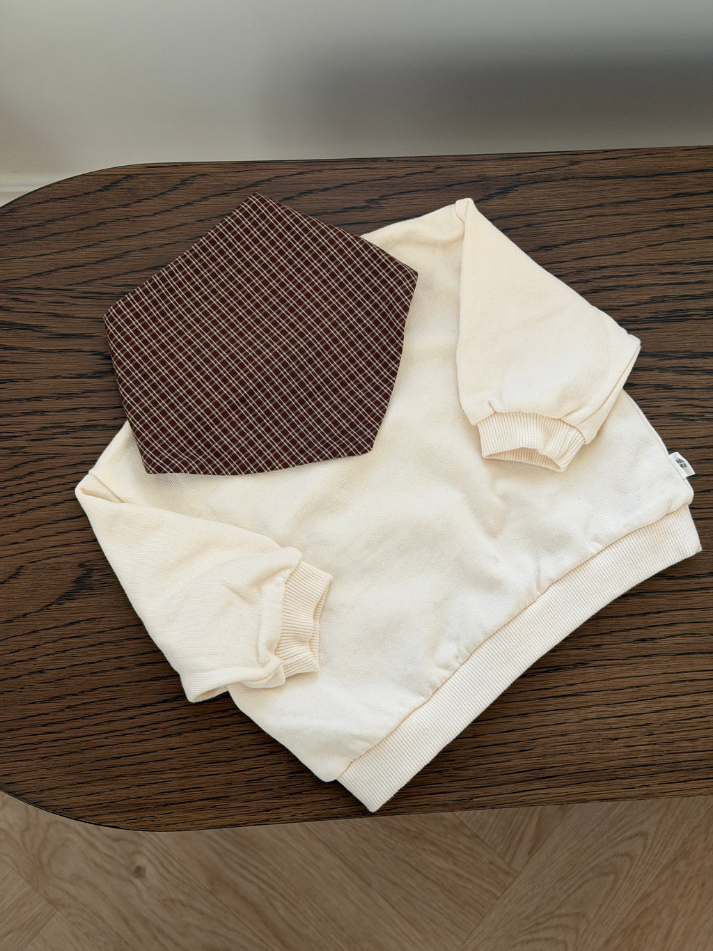 Cream crew-neck sweatshirt laid out with checked bib