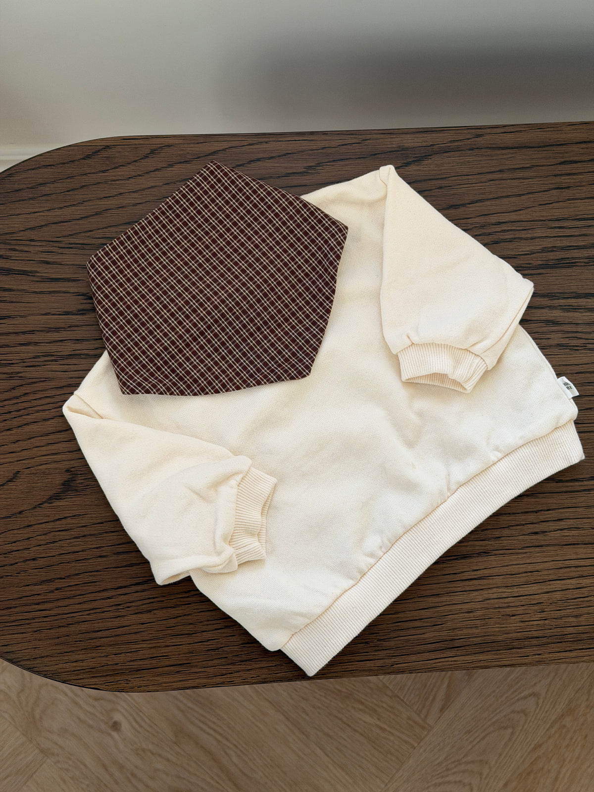 Cream crew-neck sweatshirt laid out with checked bib
