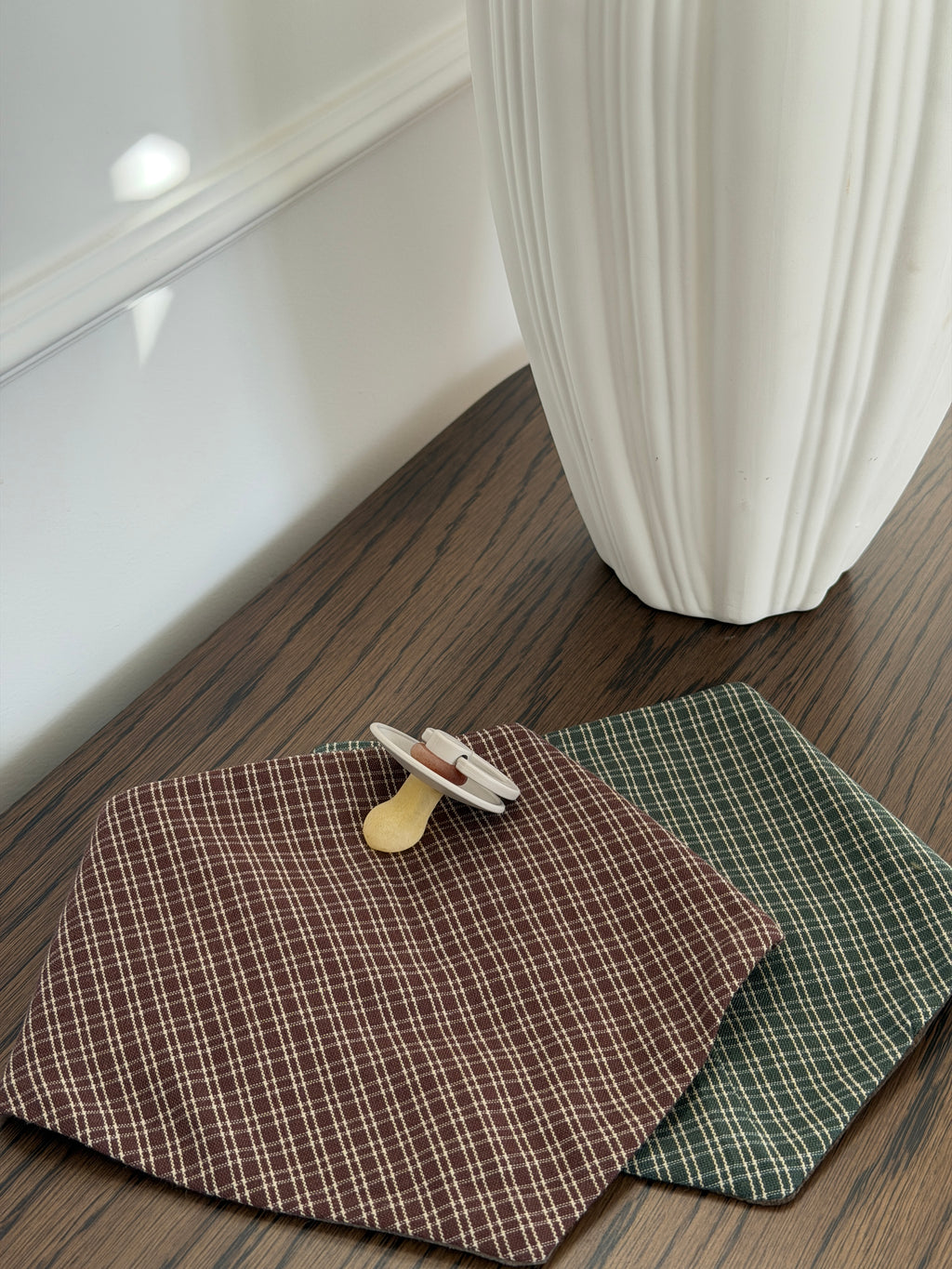Pine bib in green check and Pecan bib with a dummy on a wooden table