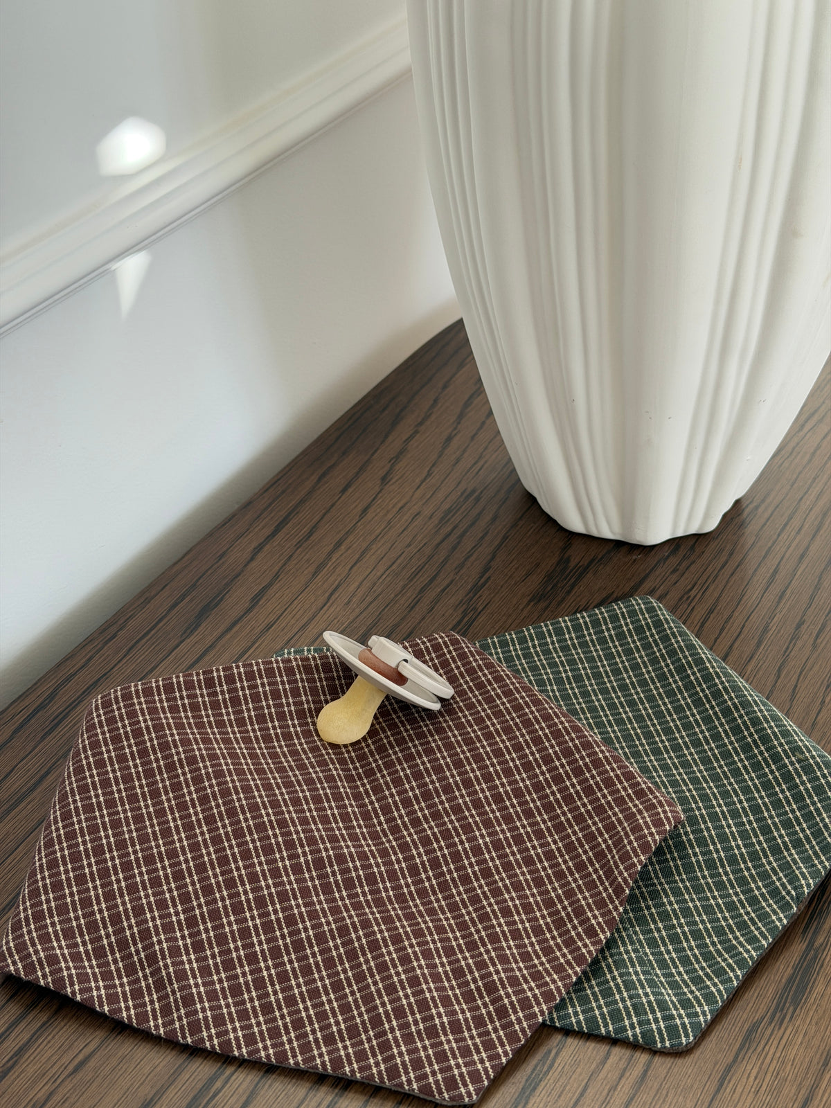 Pine bib in green check and Pecan bib with a dummy on a wooden table