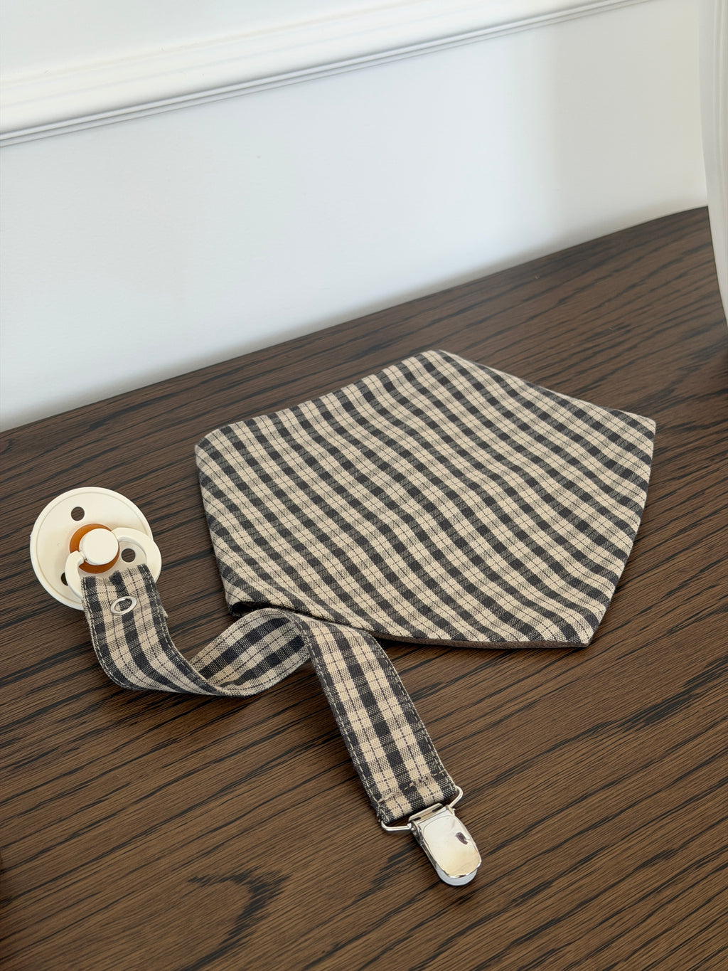 Mocca bib in brown check with a Mocca dummy clip and dummy on a wooden table