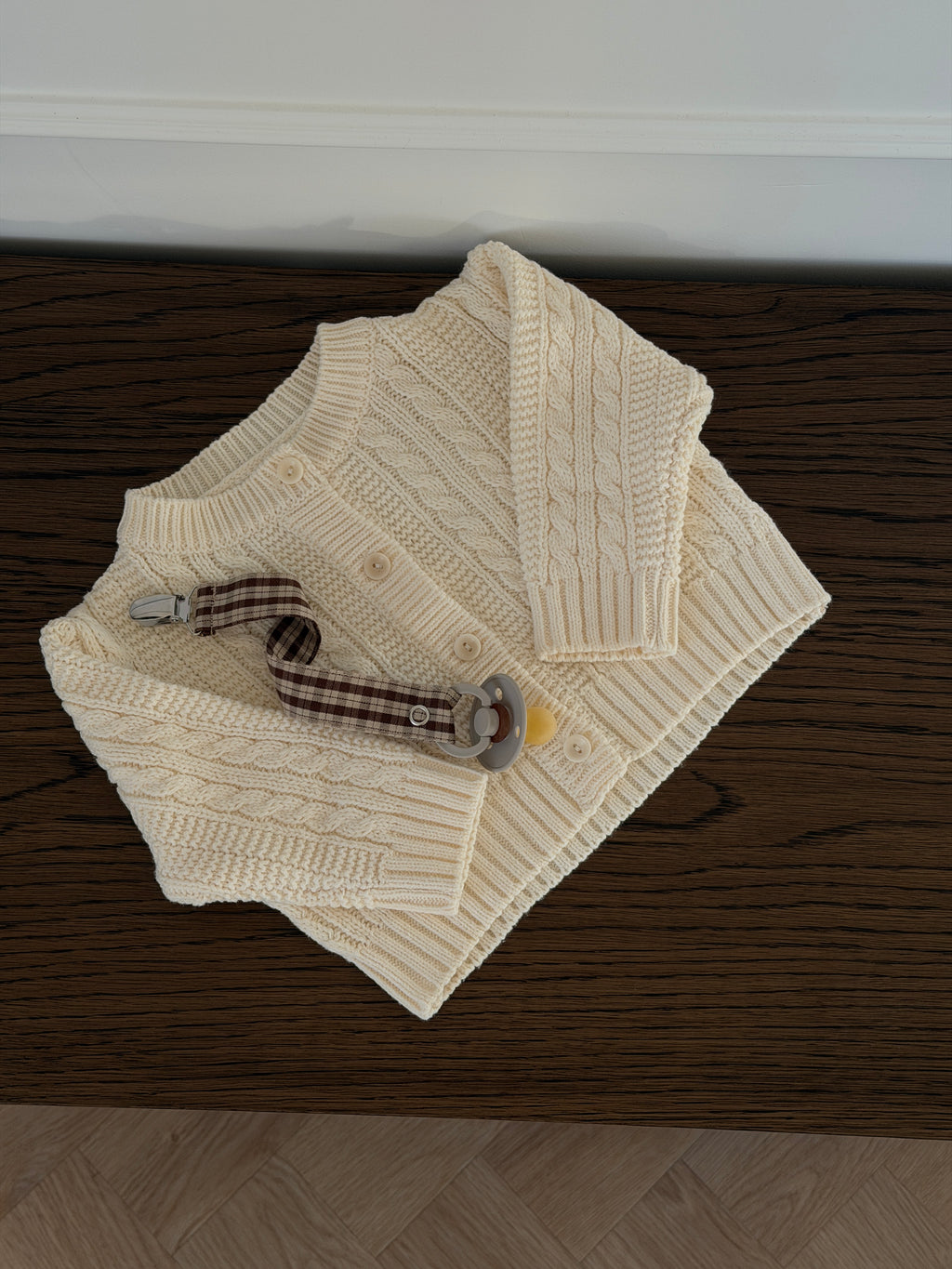 Creme kabelstrikket cardigan til baby liggende med strømper