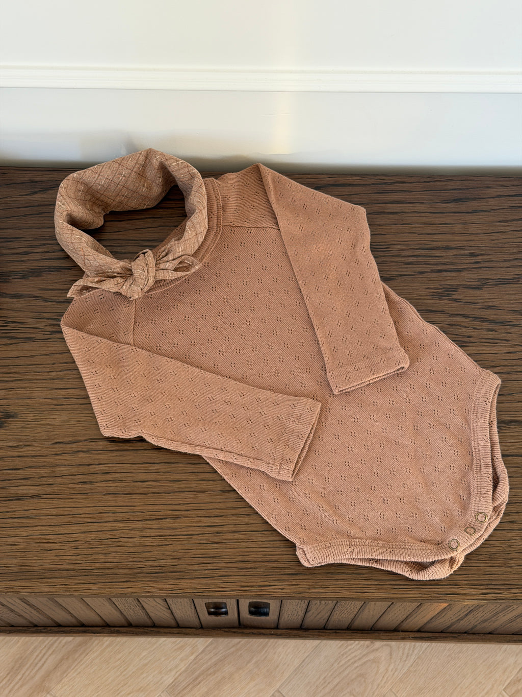 Brown long-sleeved pointelle bodysuit for baby lying on a wooden table
