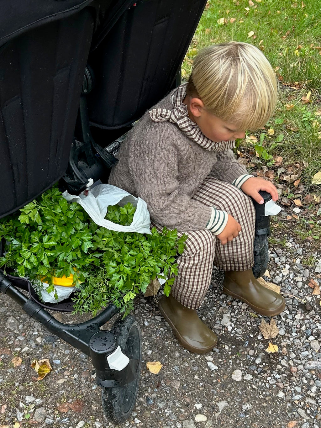 Child wearing a Cortado scarf in brown and beige check with checked trousers by a pushchair