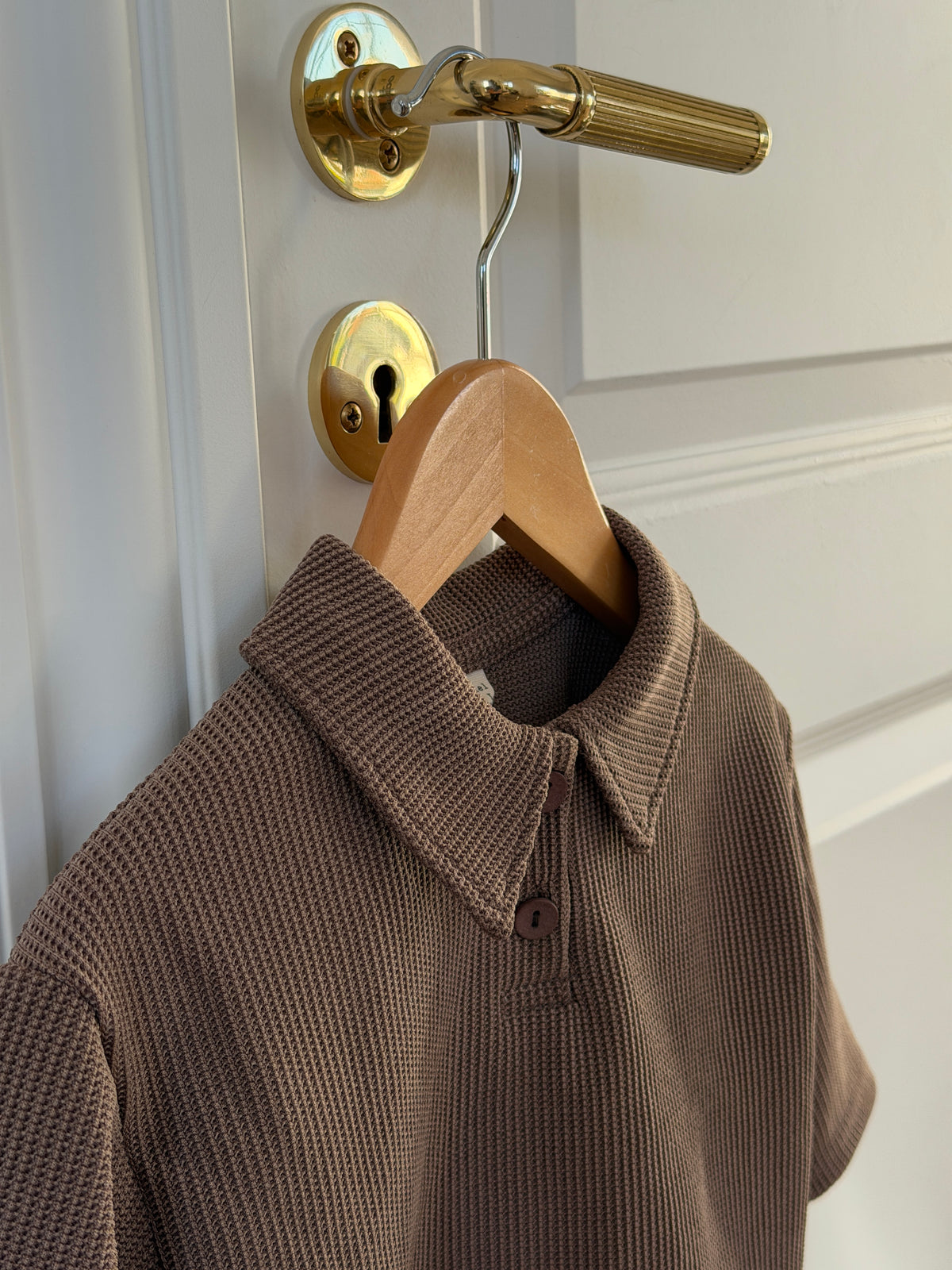Brown waffle-knit polo shirt, close-up of the collar on a hanger