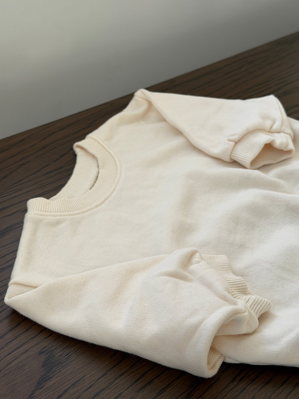 Cream crew-neck sweatshirt for baby lying on a wooden table