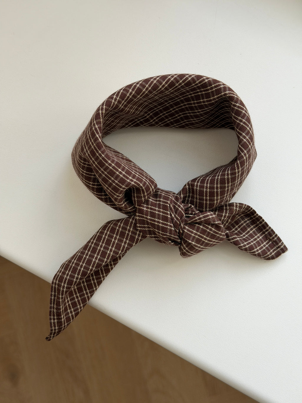 Pecan scarf in reddish-brown check cotton tied on a white table