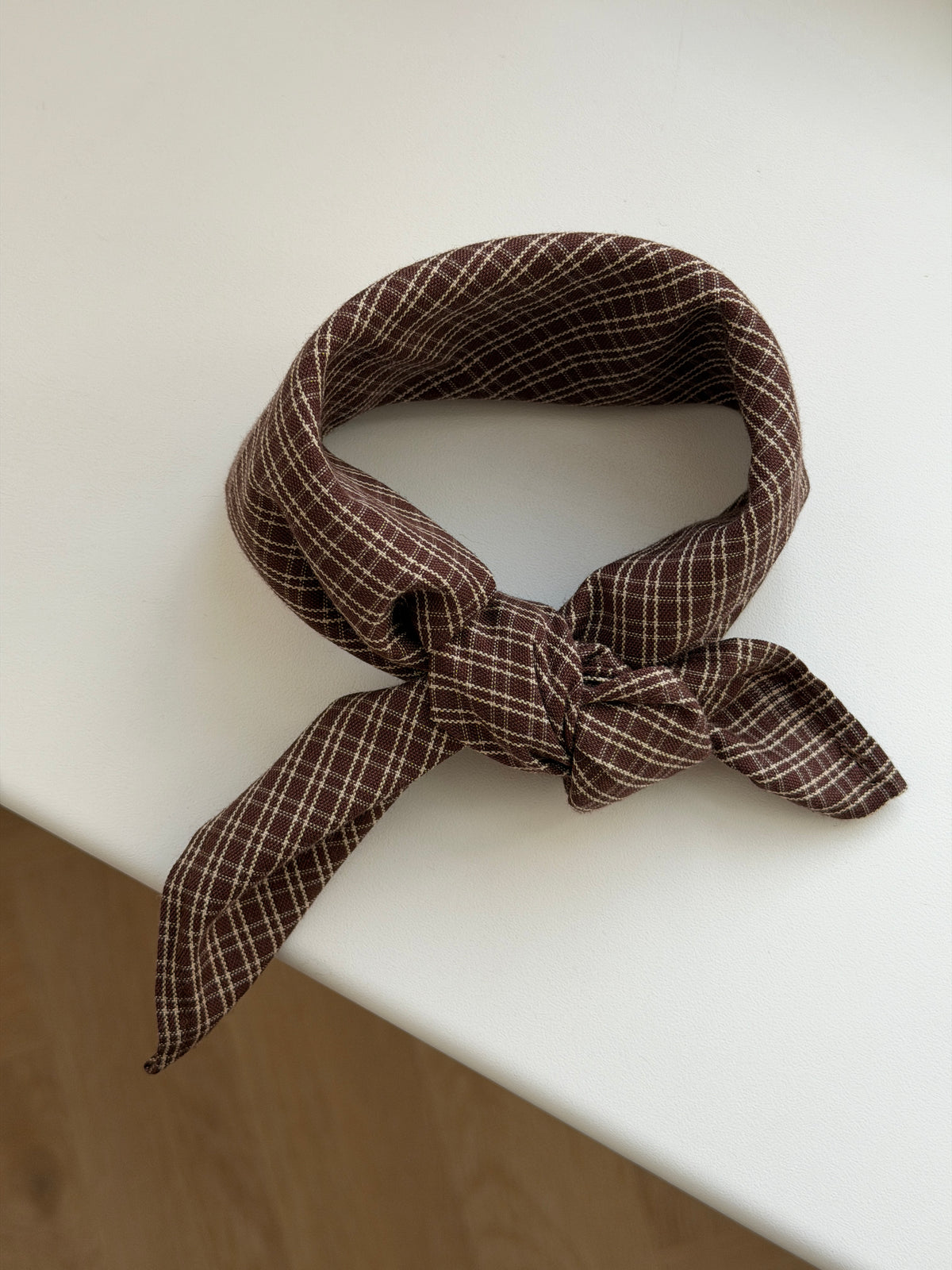 Pecan scarf in reddish-brown check cotton tied on a white table