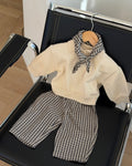 Mocca trousers in brown check cotton on a black leather chair with a cream knit top and checked scarf