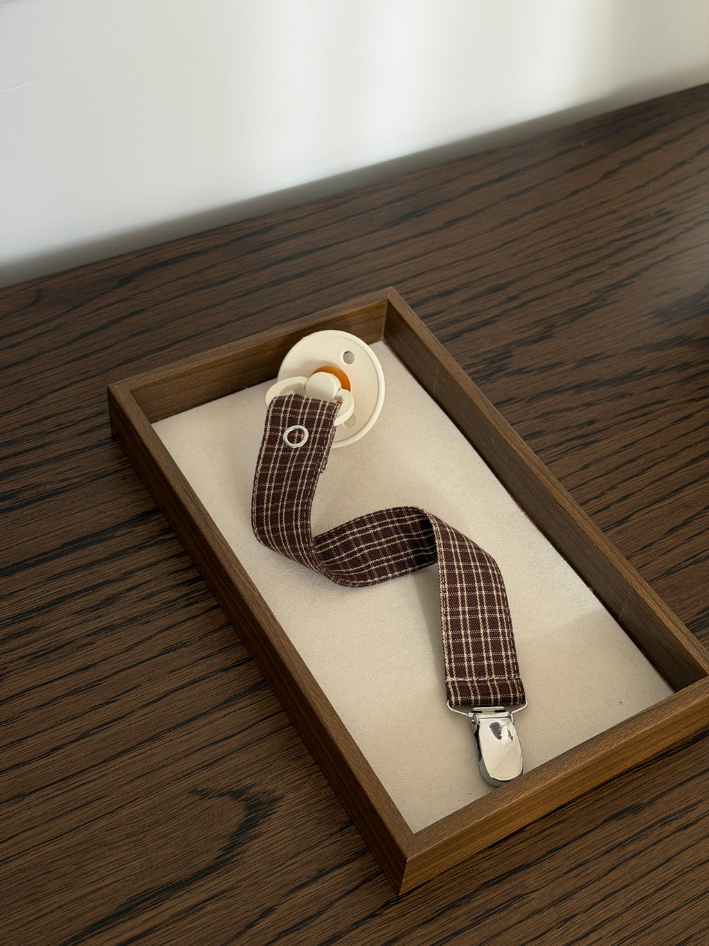 Pecan dummy clip in reddish-brown check cotton with a dummy in a wooden tray