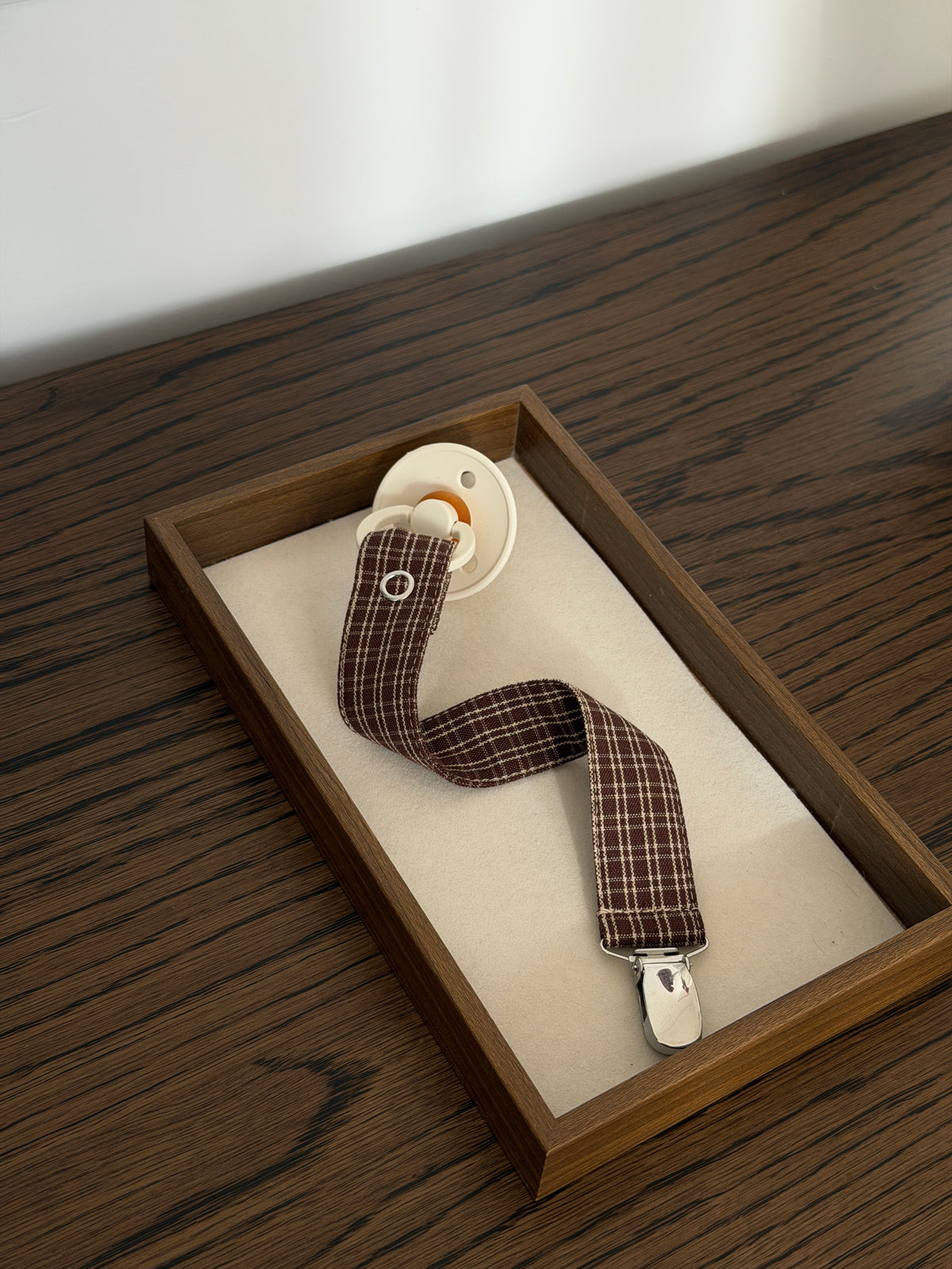 Pecan dummy clip in reddish-brown check cotton with a dummy in a wooden tray