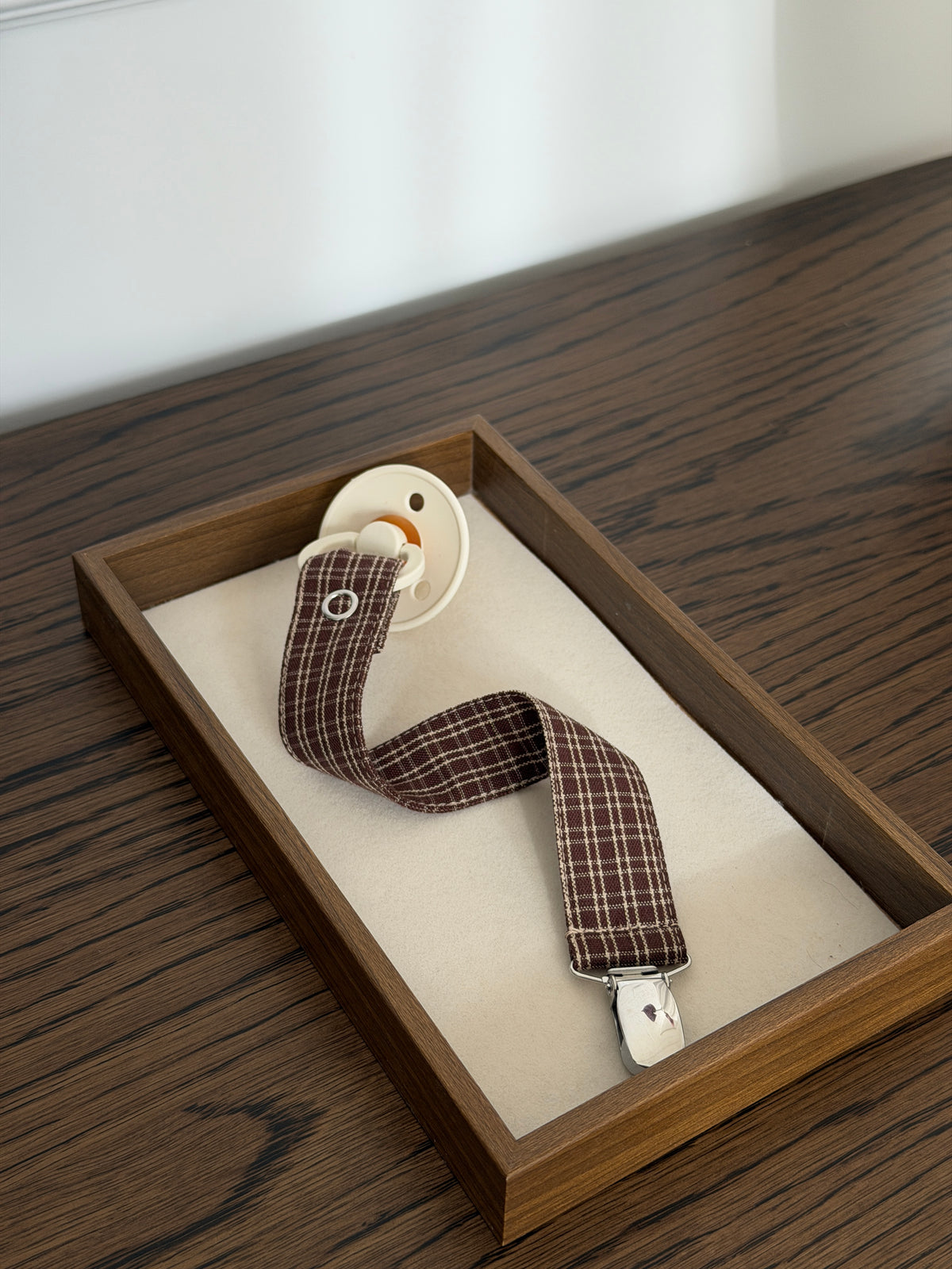 Pecan dummy clip in reddish-brown check with a dummy and metal clip in a wooden tray on a table