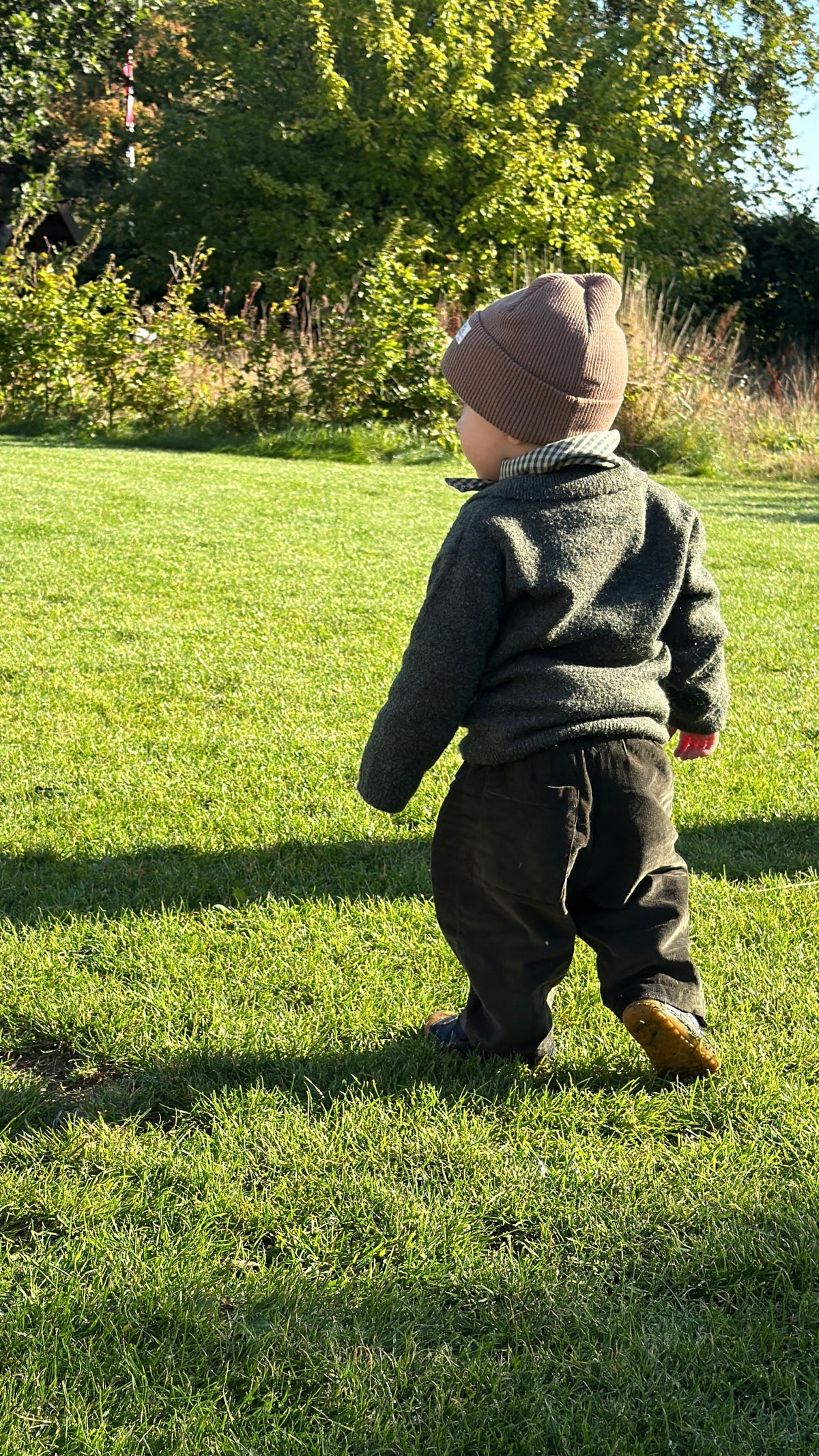 Child walking in the garden in Olive needlecord trousers and Matcha mini scarf