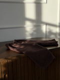 Brown velvet baby trousers folded on a dark wooden sideboard in sunlight