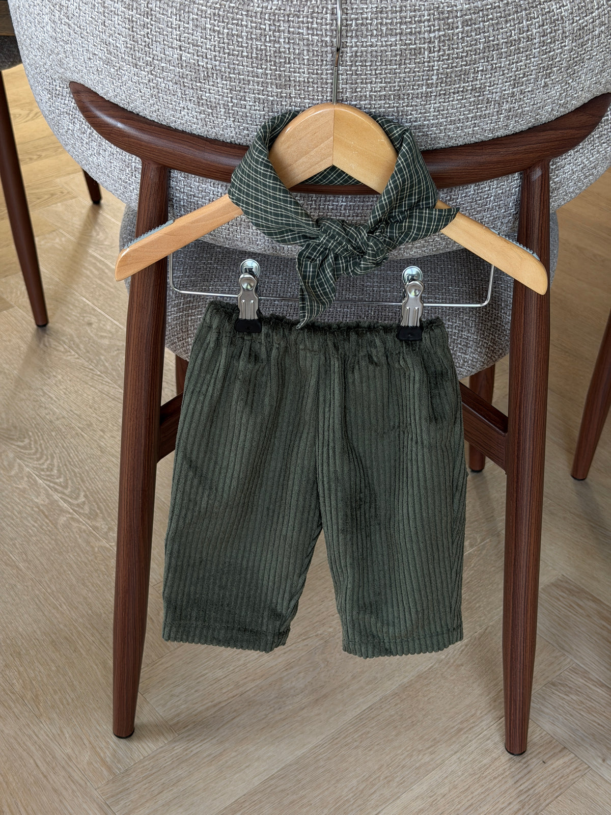Green velvet trousers and a green checked scarf on a hanger over an upholstered chair