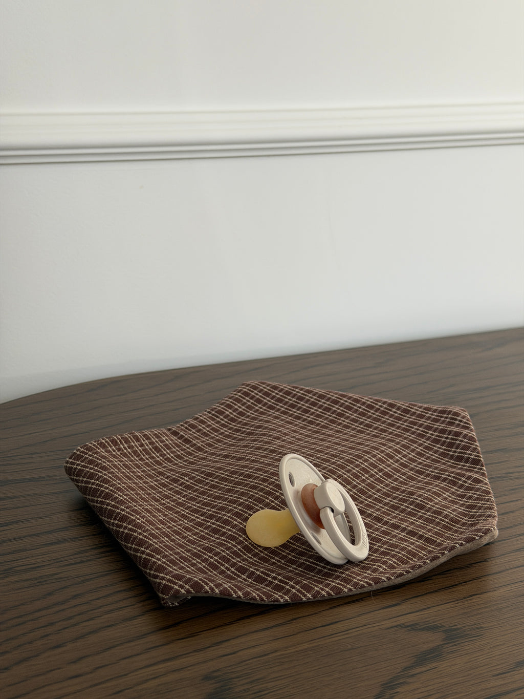 Pecan bib in reddish-brown check cotton with a dummy on a wooden table