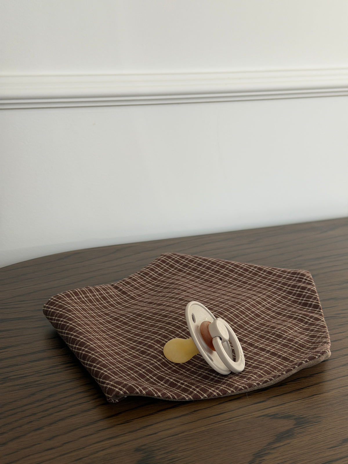 Pecan bib in reddish-brown check cotton with a dummy on a wooden table