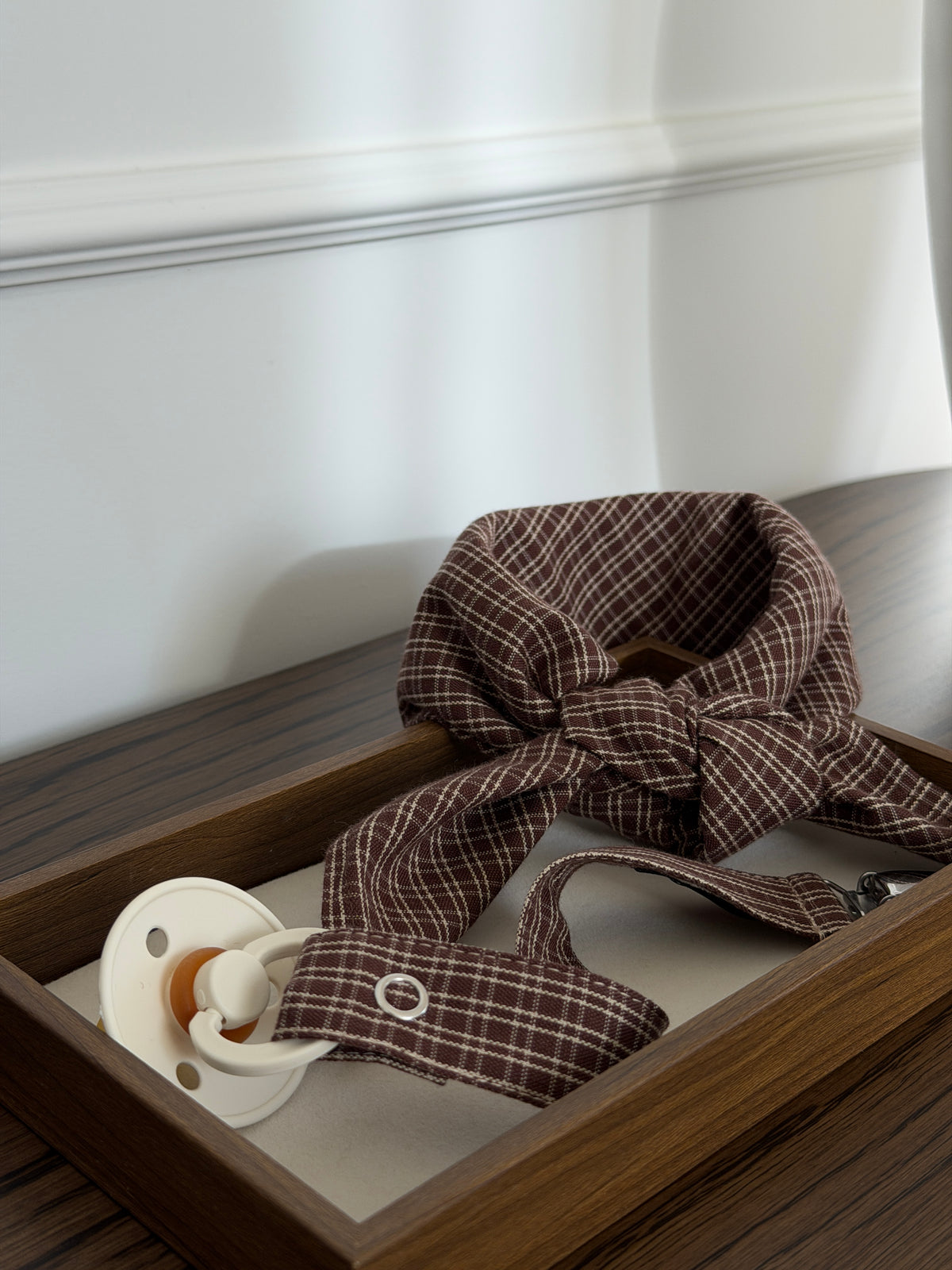 Pecan scarf in reddish-brown check with a dummy clip and dummy in a wooden tray on a table