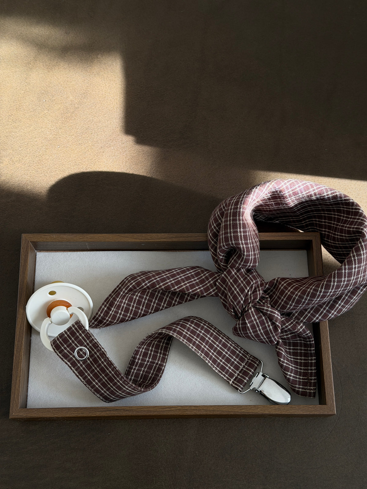 Pecan scarf and dummy clip in reddish-brown check with a dummy in a wooden tray in sunlight