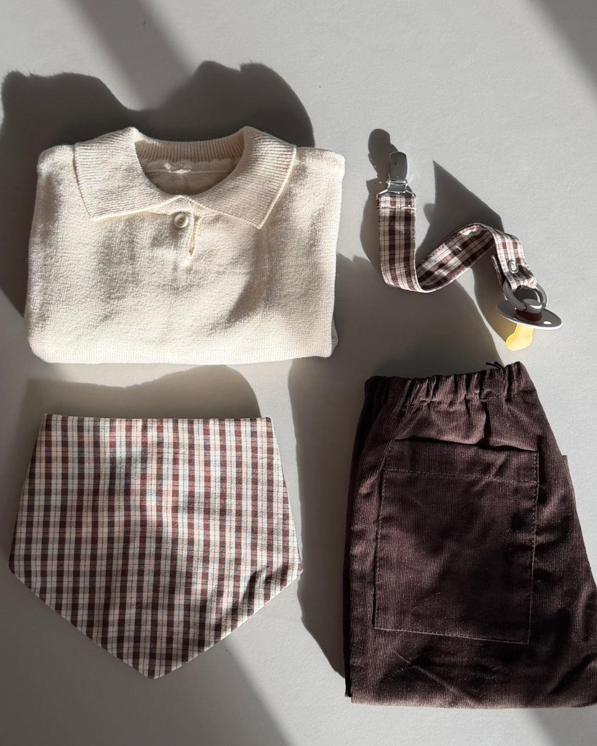 Creme strikket polotrøje – flatlay med hagesmæk og bukser