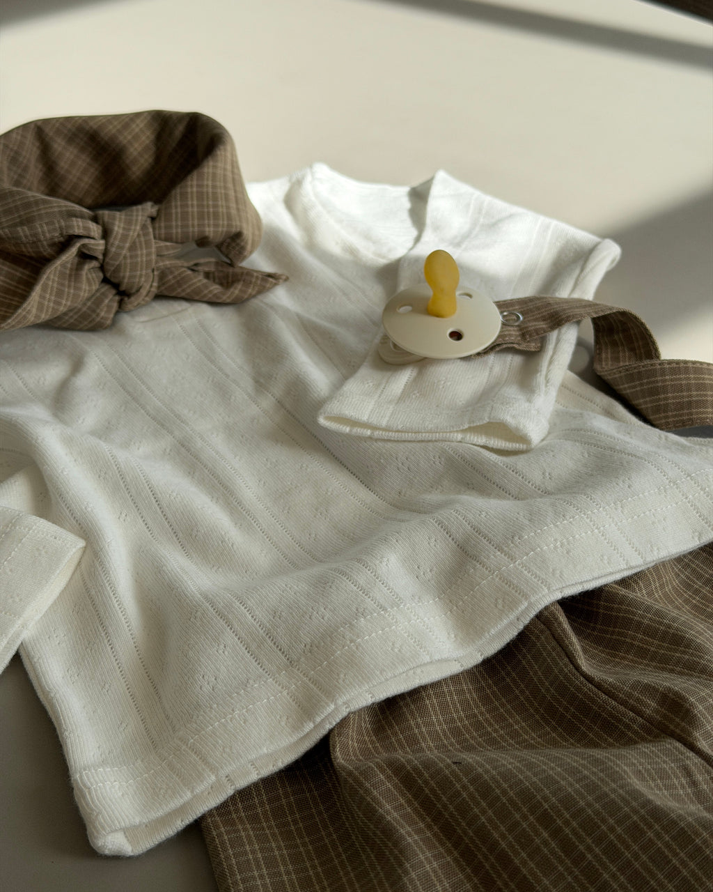 Cream pointelle top with buttons laid out with scarf and brown trousers