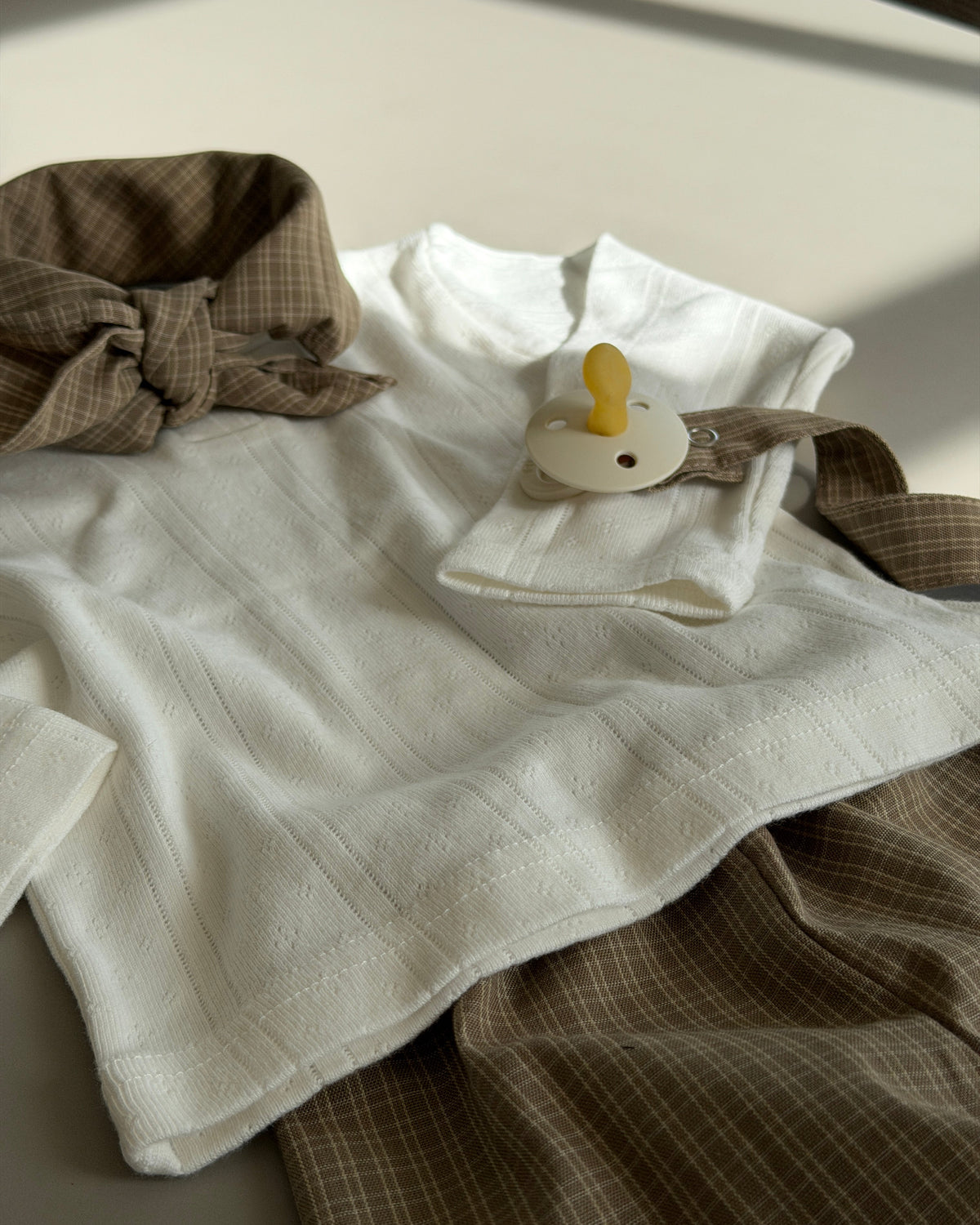 Cream pointelle top with buttons laid out with scarf and brown trousers