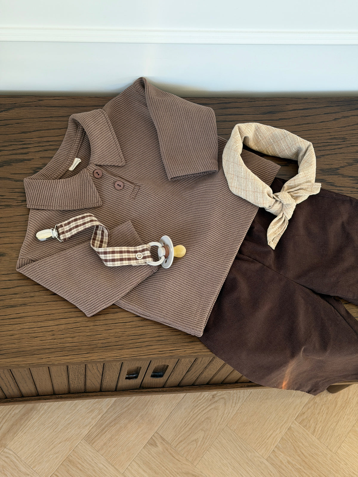 Brown waffle-knit polo shirt laid out with trousers and scarf