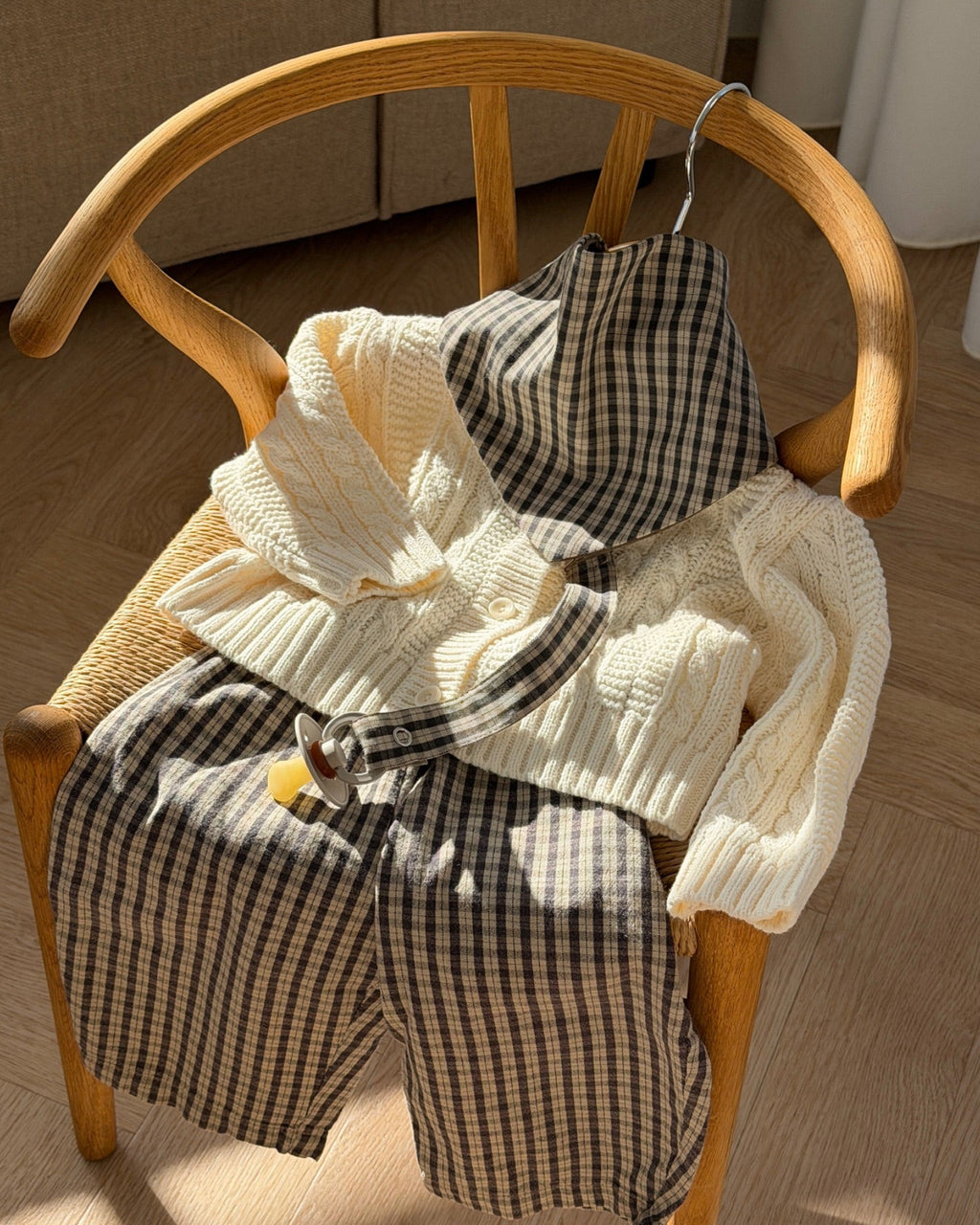 Mocca bib in brown check cotton on a chair with knit and trousers