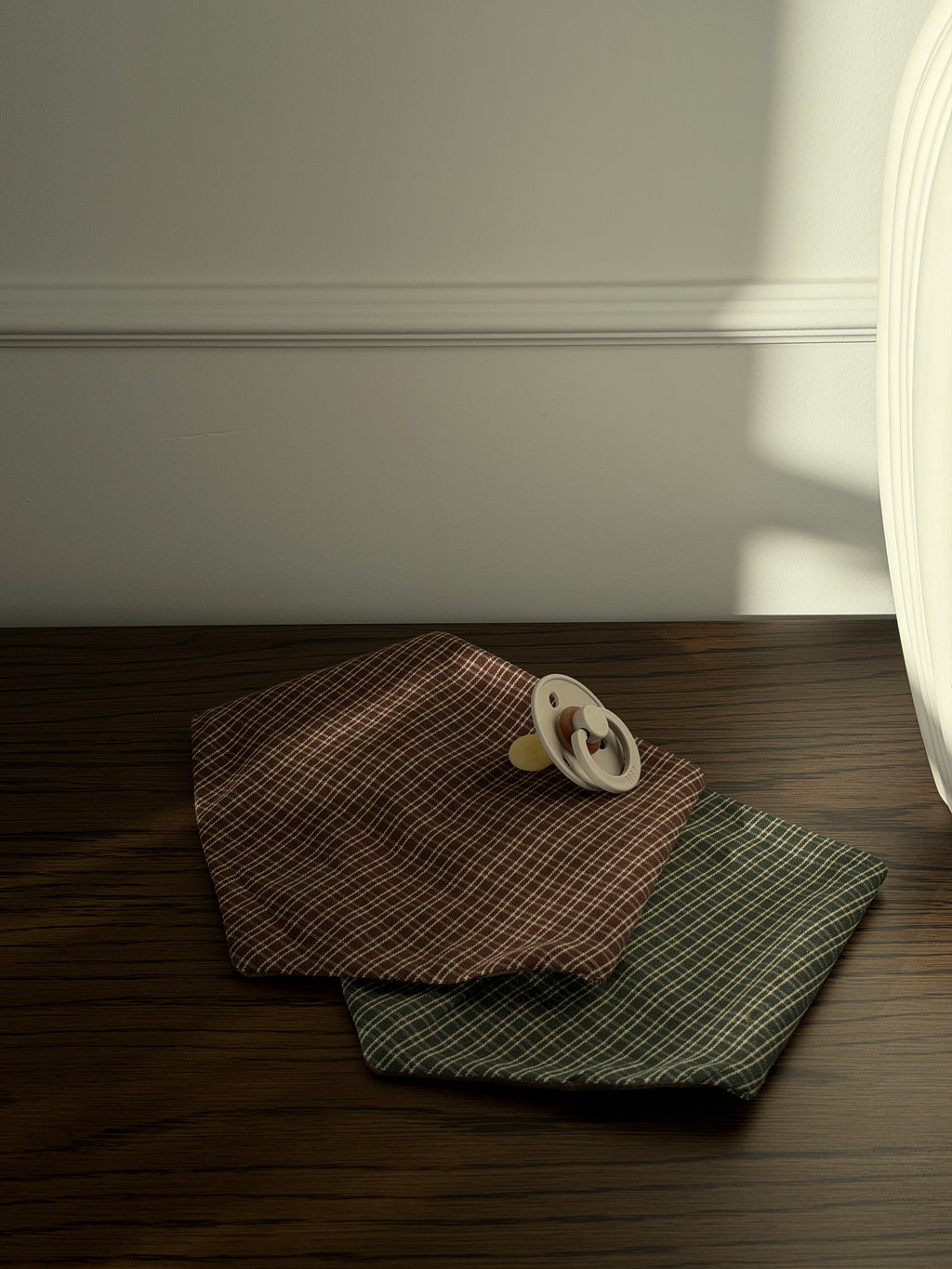 Pine bib in green check under a Pecan bib with a dummy on a dark wooden table