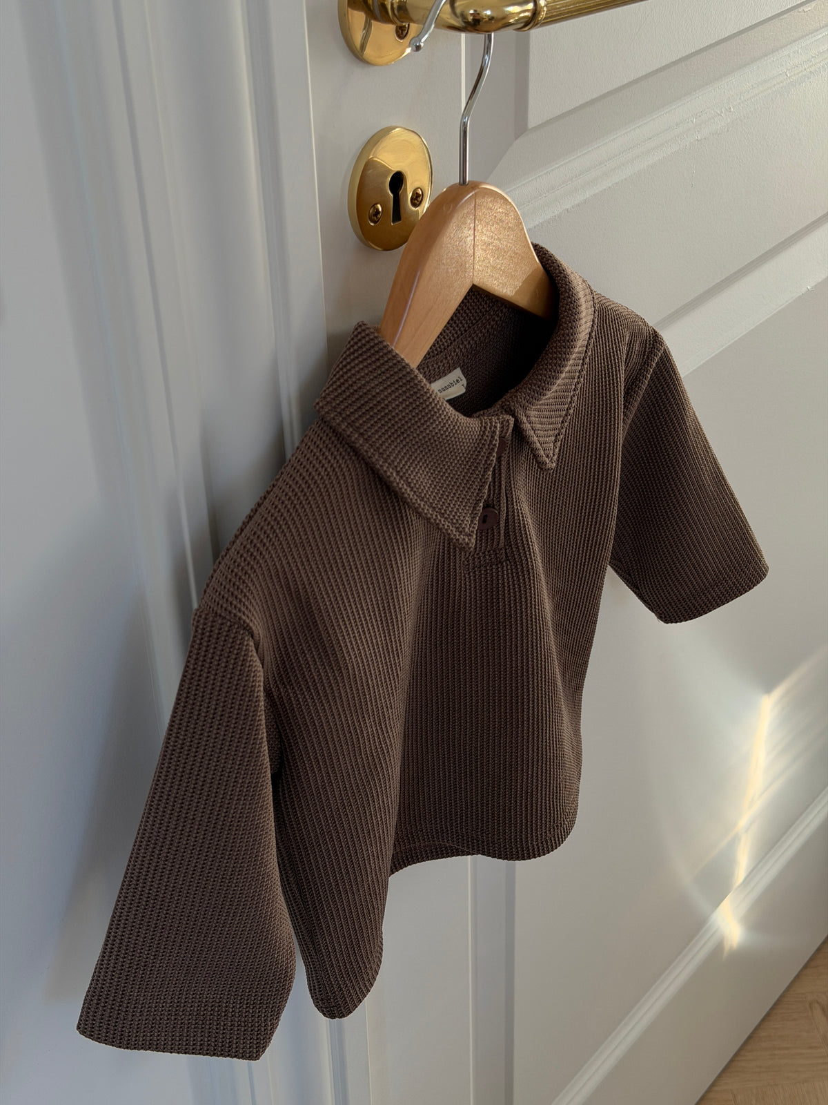 Brown waffle-knit polo shirt on a hanger on a door