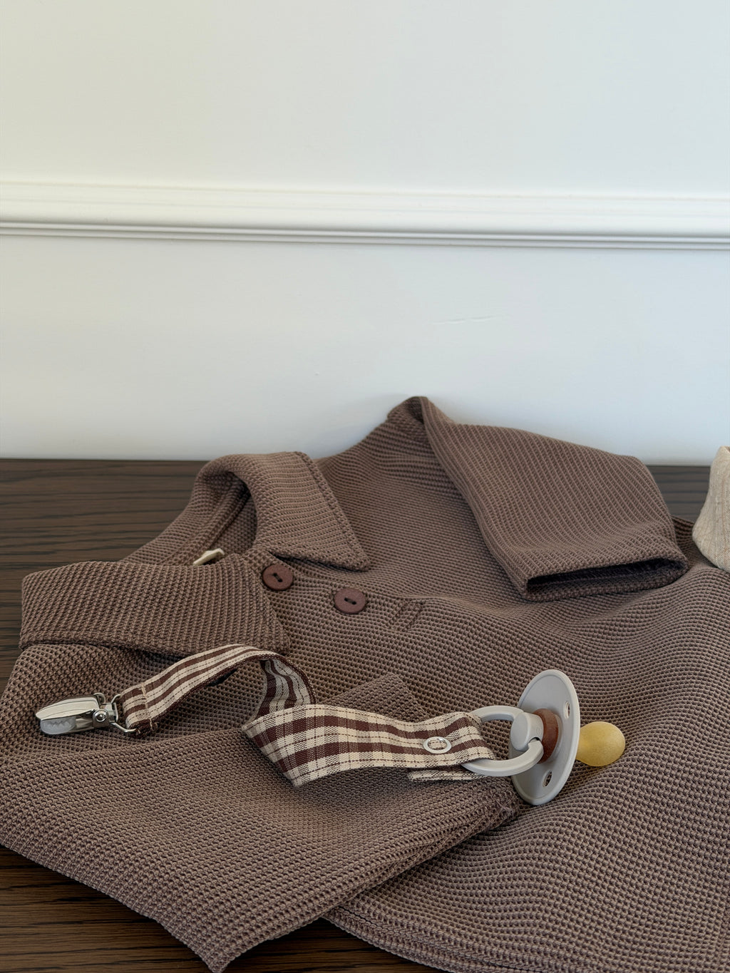 Brown waffle-knit polo shirt for baby laid out with scarf and dummy clip