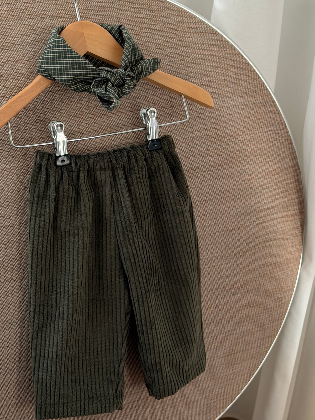 Green velvet trousers with a green checked scarf on a hanger on a round table