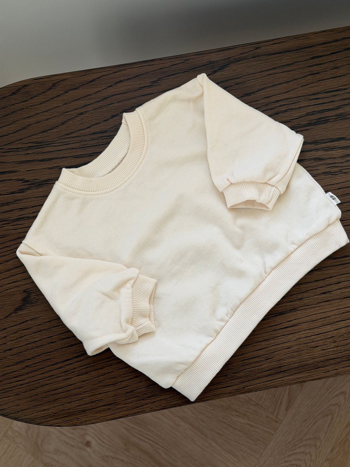 Cream crew-neck sweatshirt lying on a wooden table
