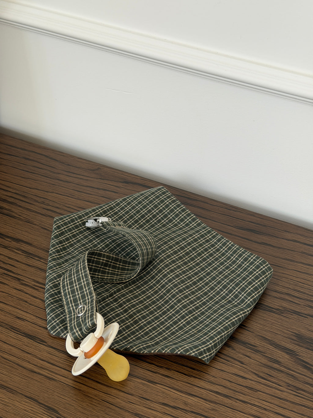 Pine bib in green check cotton with a Pine dummy clip and dummy on a wooden table