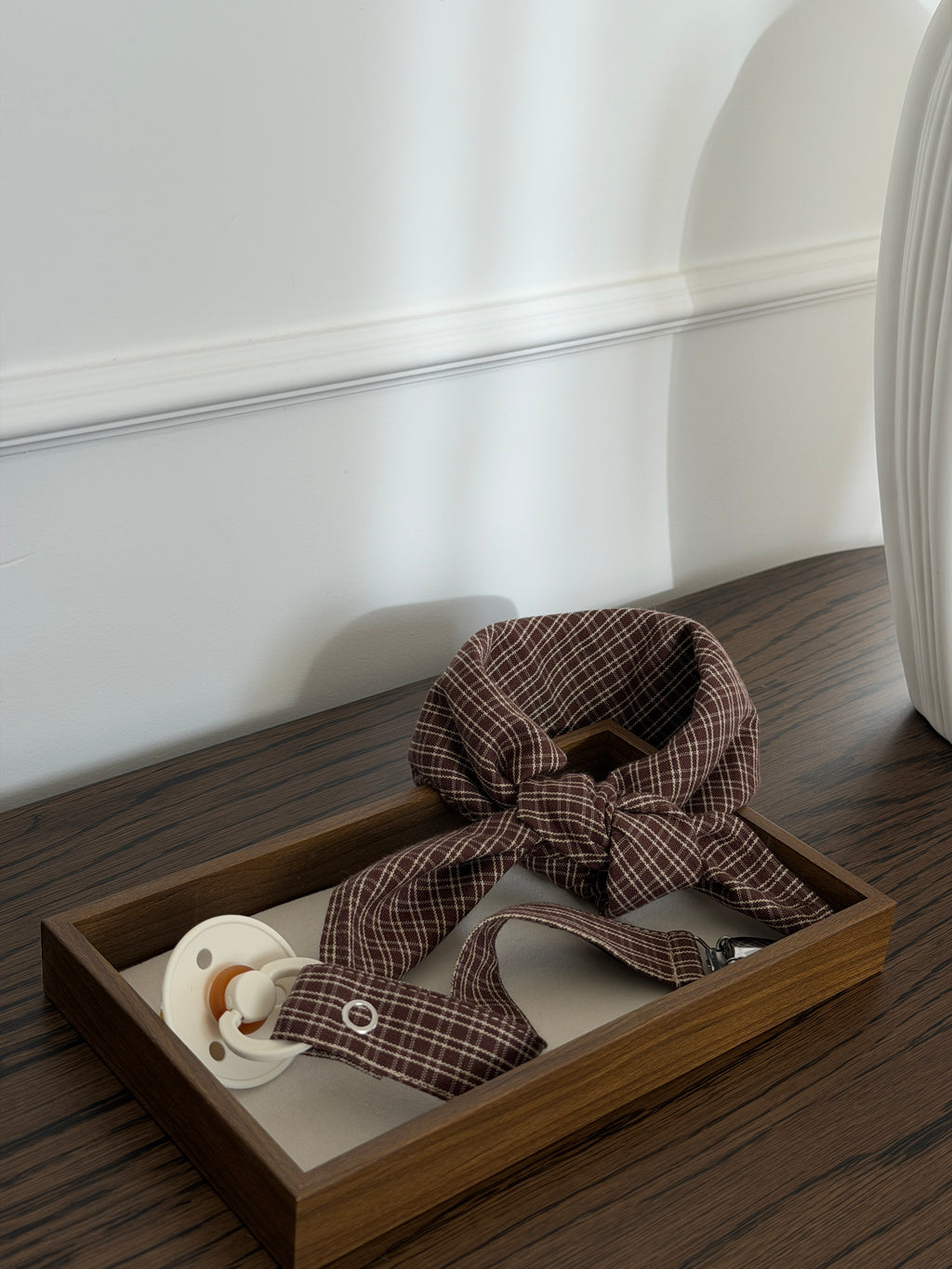 Pecan scarf and dummy clip in reddish-brown check in a wooden tray by a white vase