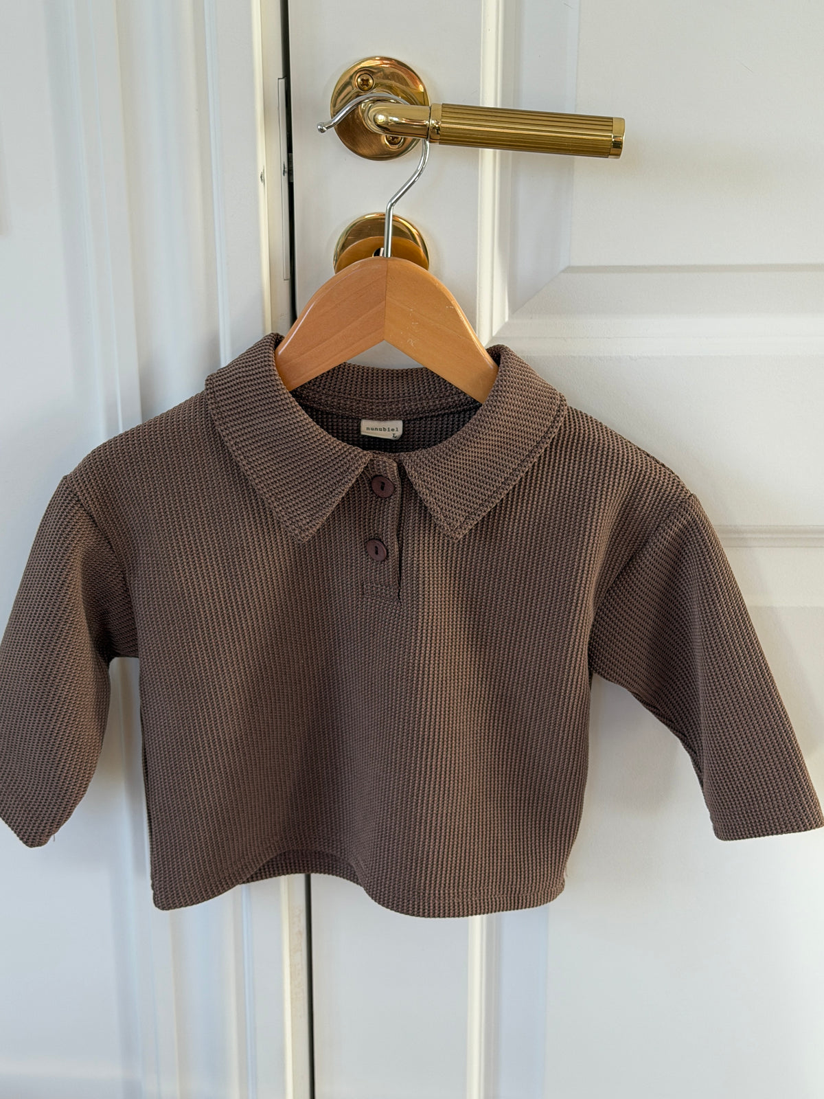 Brown waffle-knit polo shirt for baby on a hanger on a door