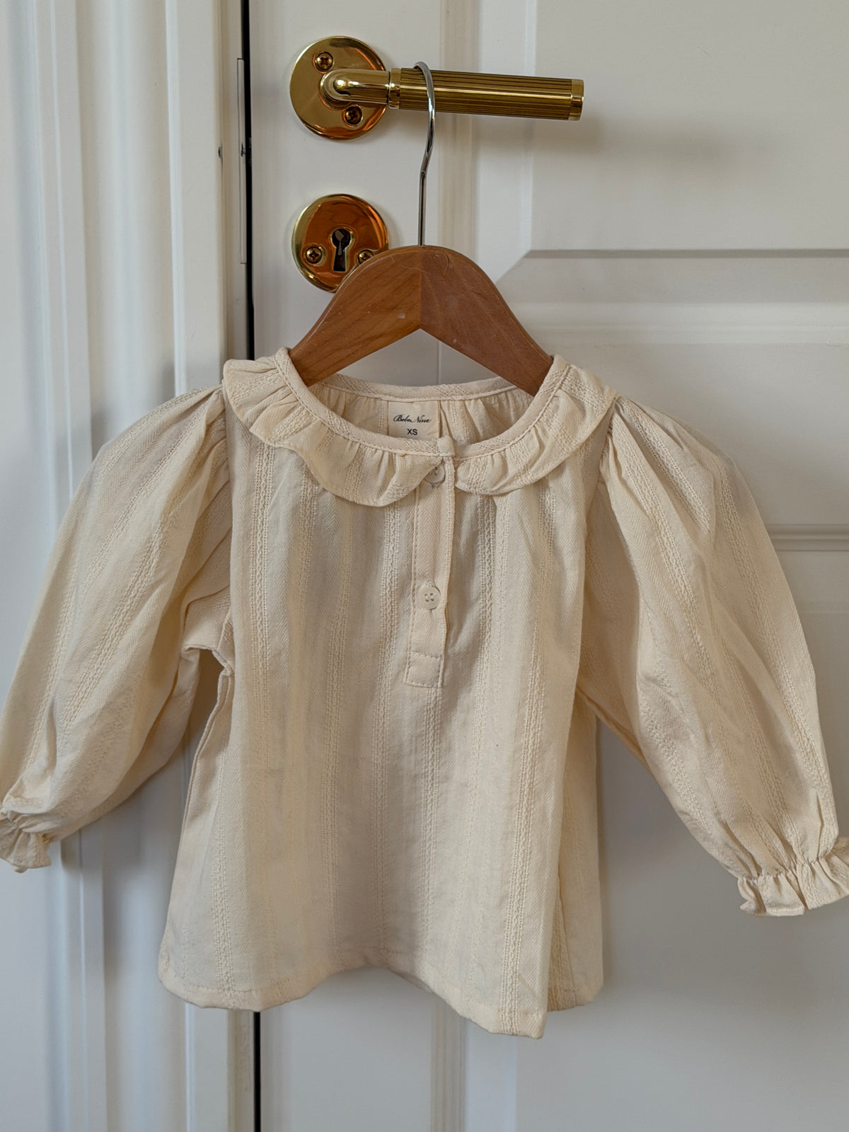 Creme skjortebluse med flæsekrave på bøjle på dør