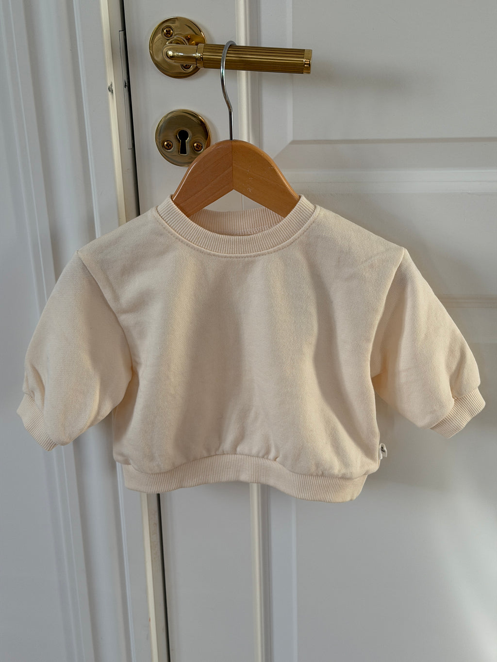 Cream crew-neck sweatshirt on a hanger on a door
