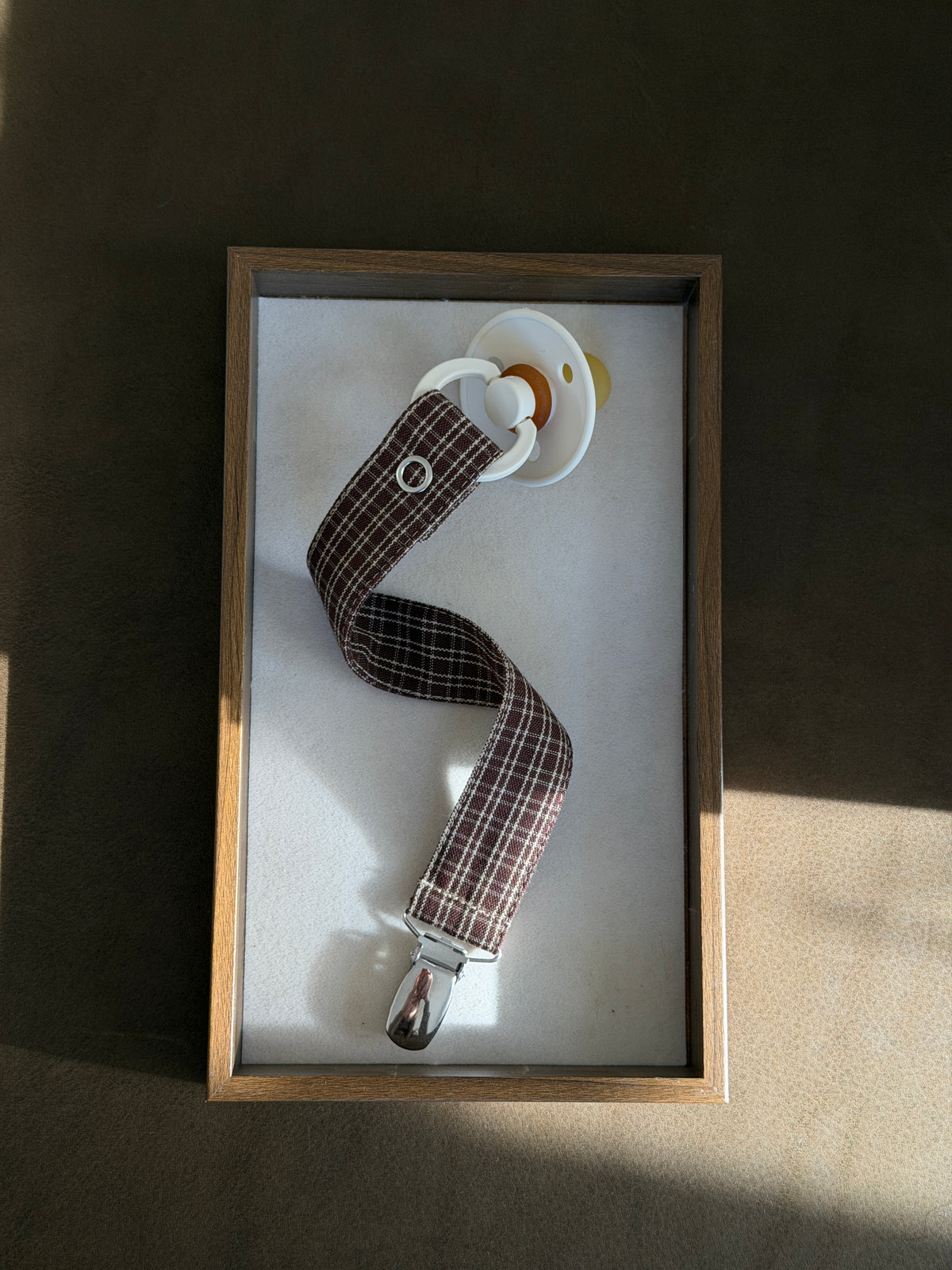 Pecan dummy clip in reddish-brown check cotton with a dummy in a wooden tray, seen from above