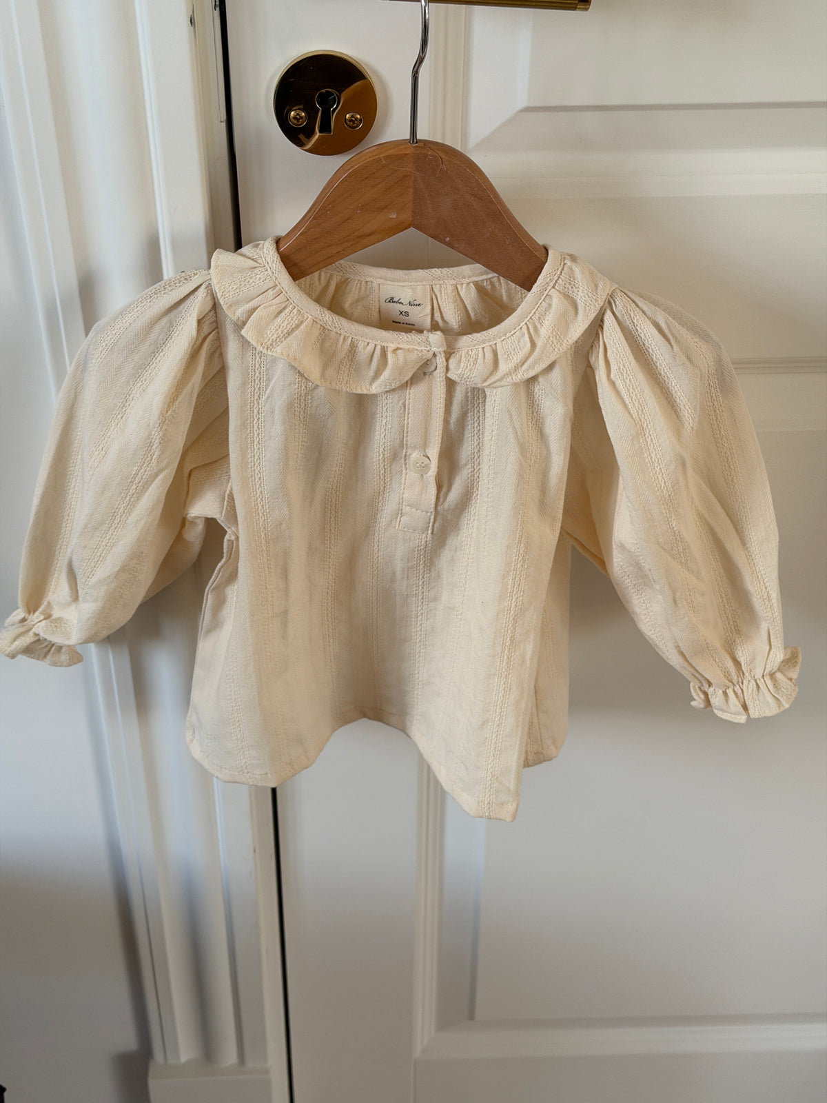 Creme skjortebluse med flæsekrave til baby på bøjle på dør