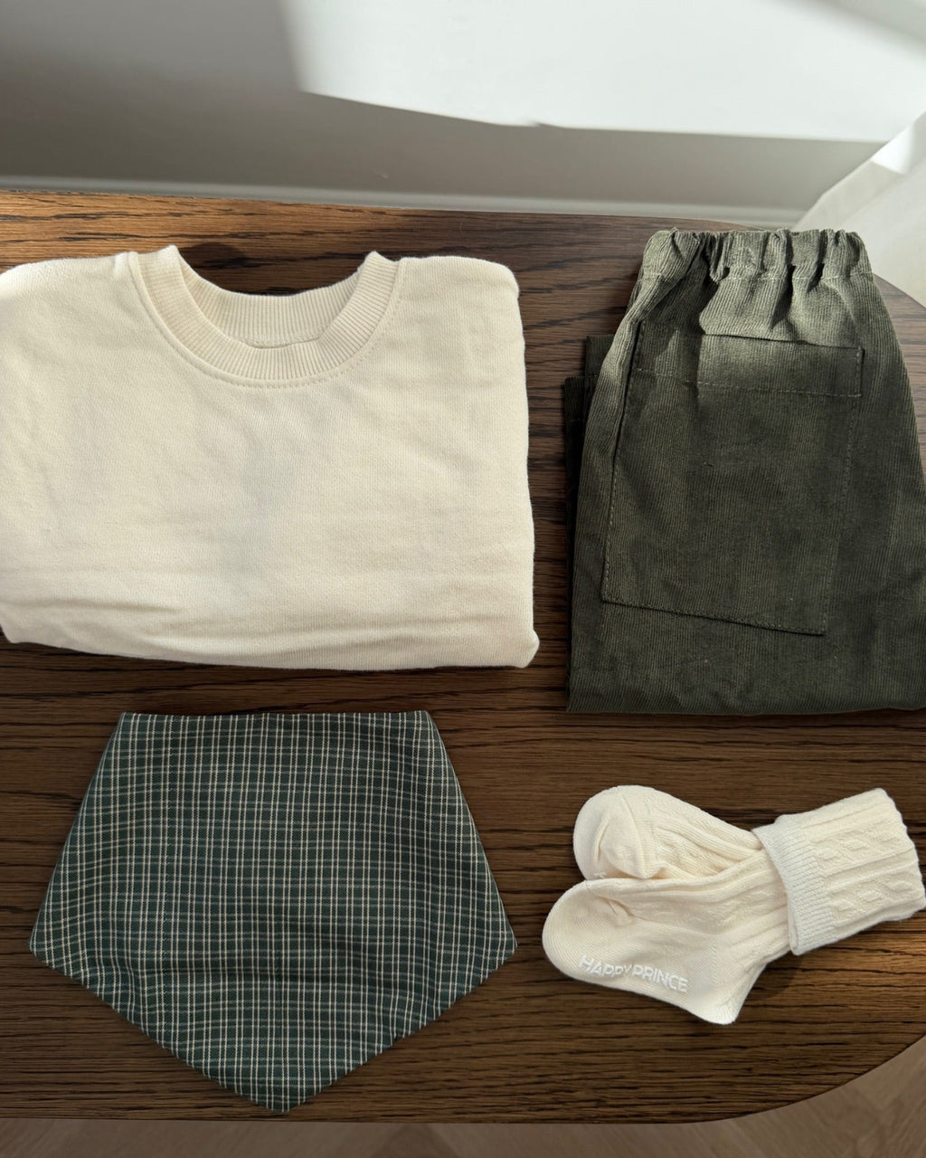 Cream crew-neck sweatshirt laid out with green trousers, bib and socks