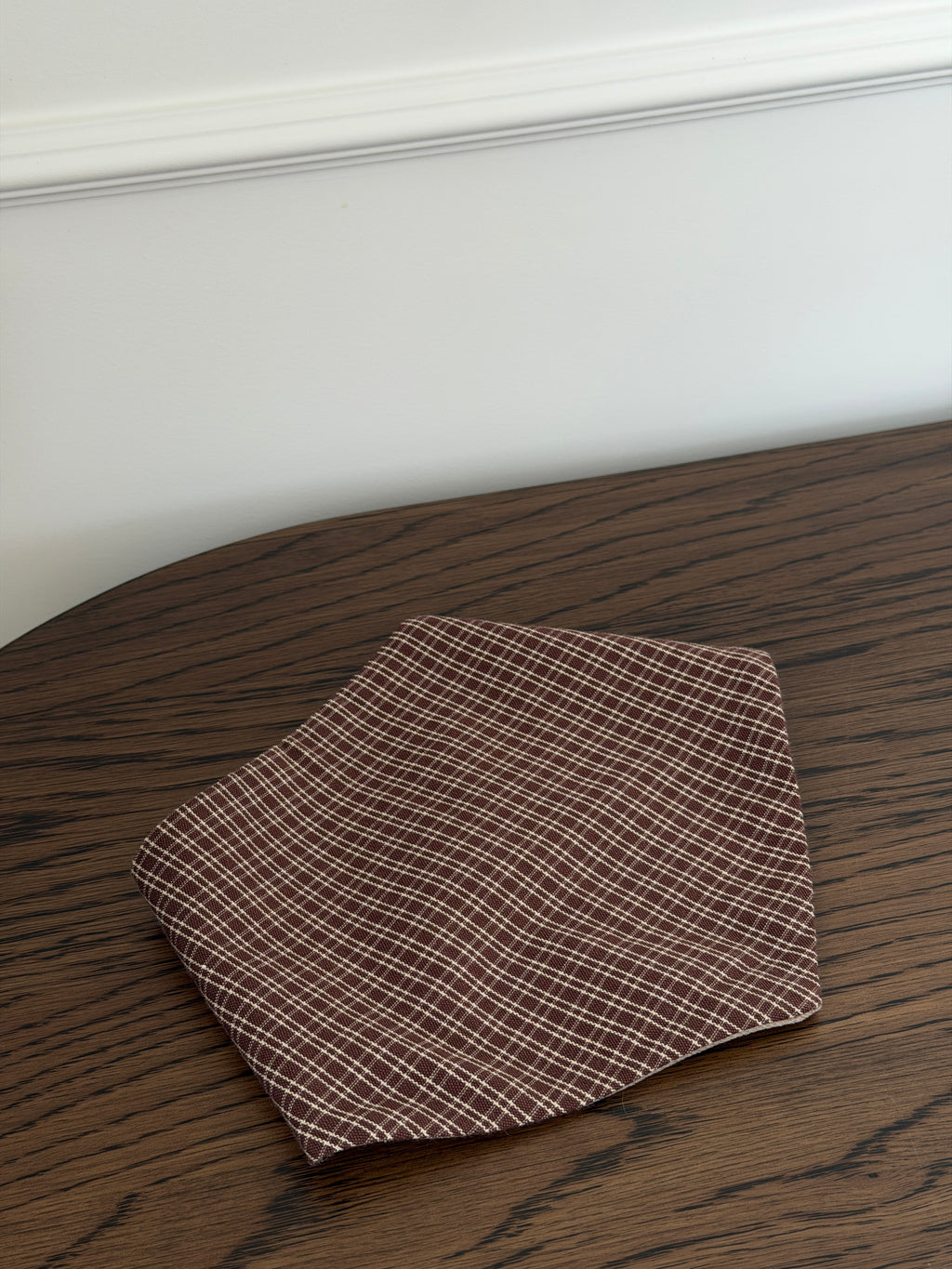 Pecan bib in reddish-brown check cotton on a dark wooden table