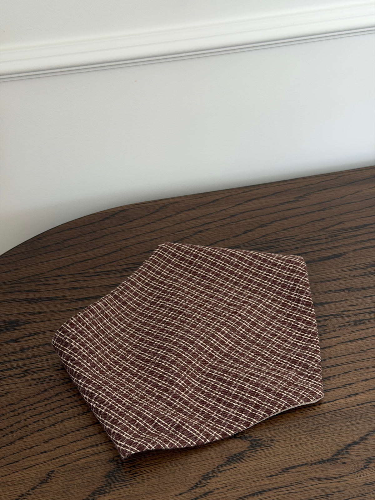 Pecan bib in reddish-brown check cotton on a dark wooden table