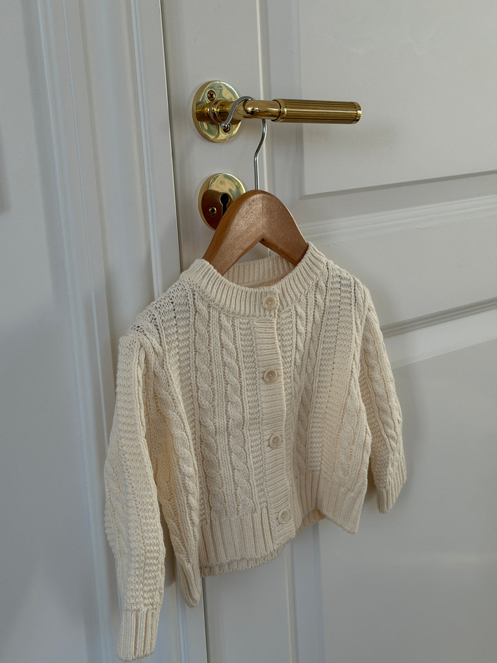 Creme kabelstrikket cardigan på bøjle på dør