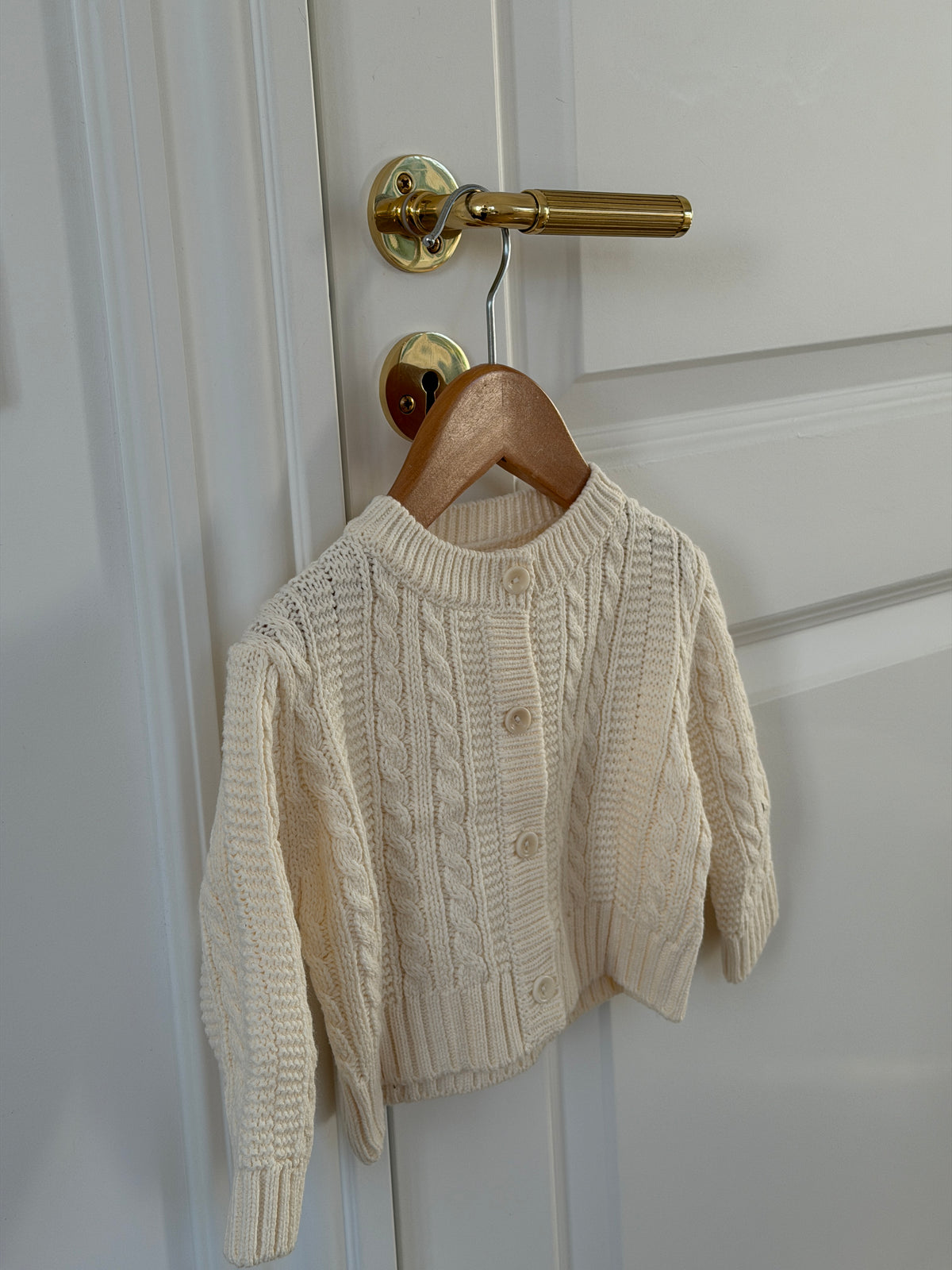Creme kabelstrikket cardigan på bøjle på dør
