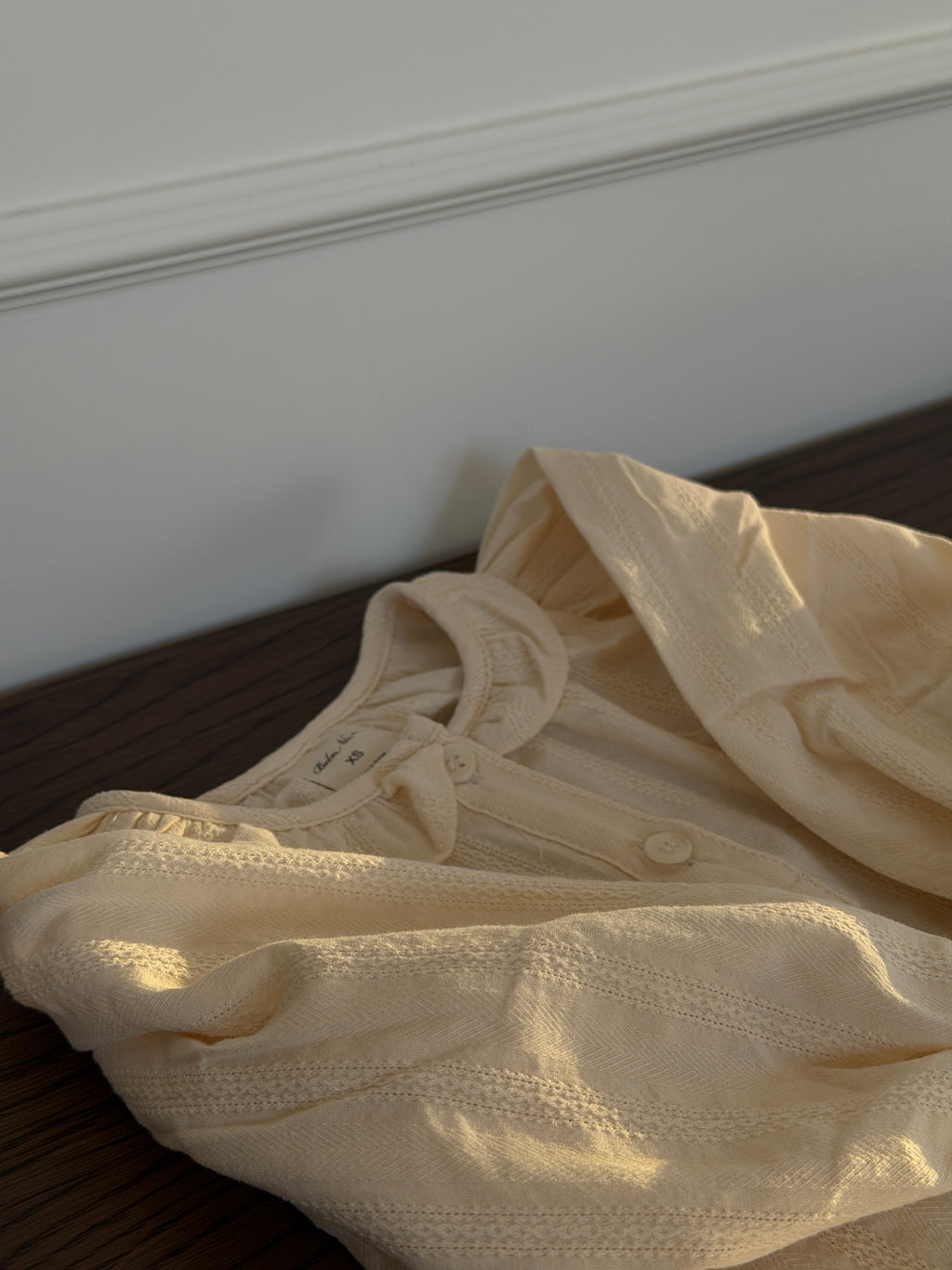 Creme skjortebluse med flæsekrave liggende på sofa