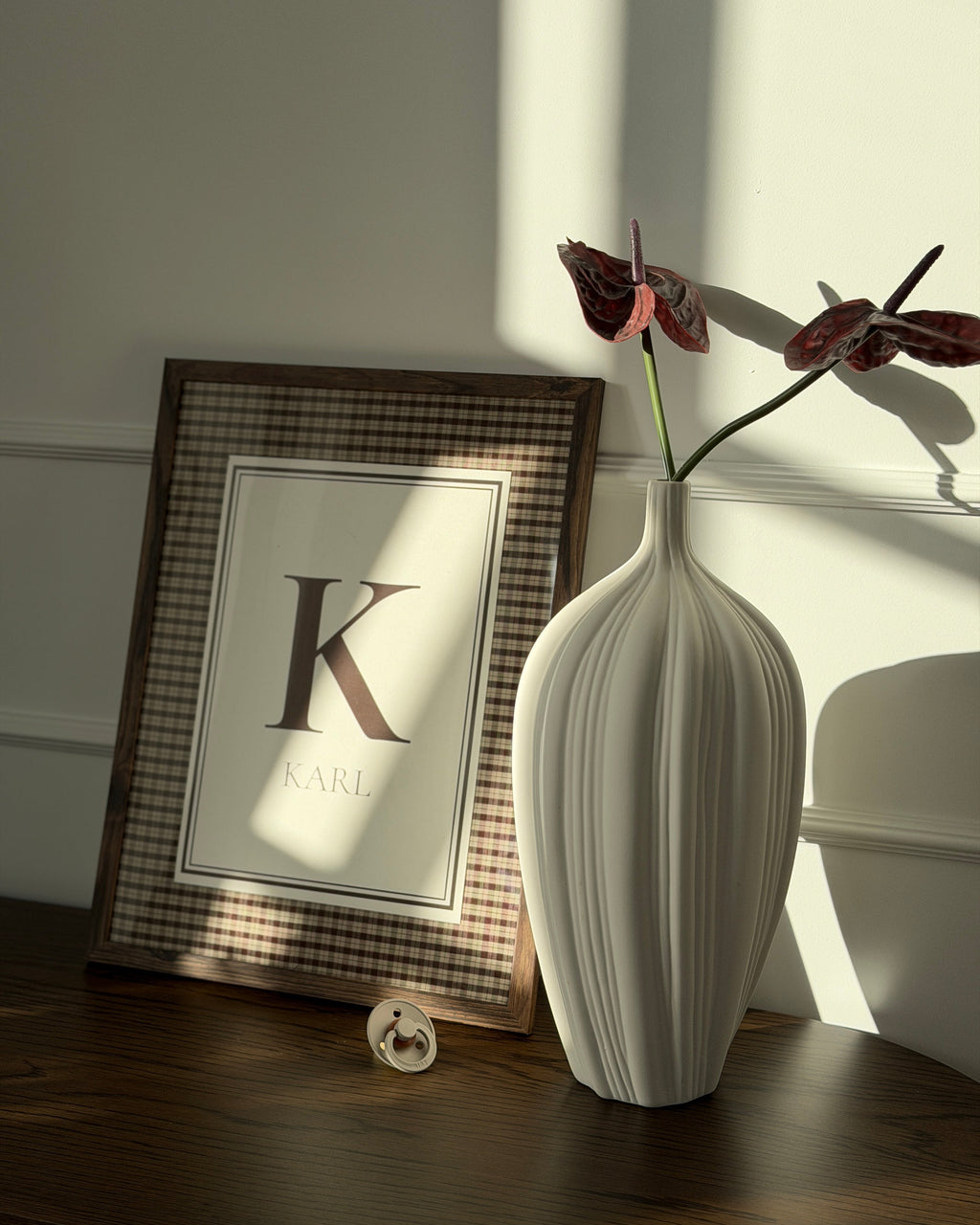 Cortado name poster with initial and name in a dark wooden frame by a white vase