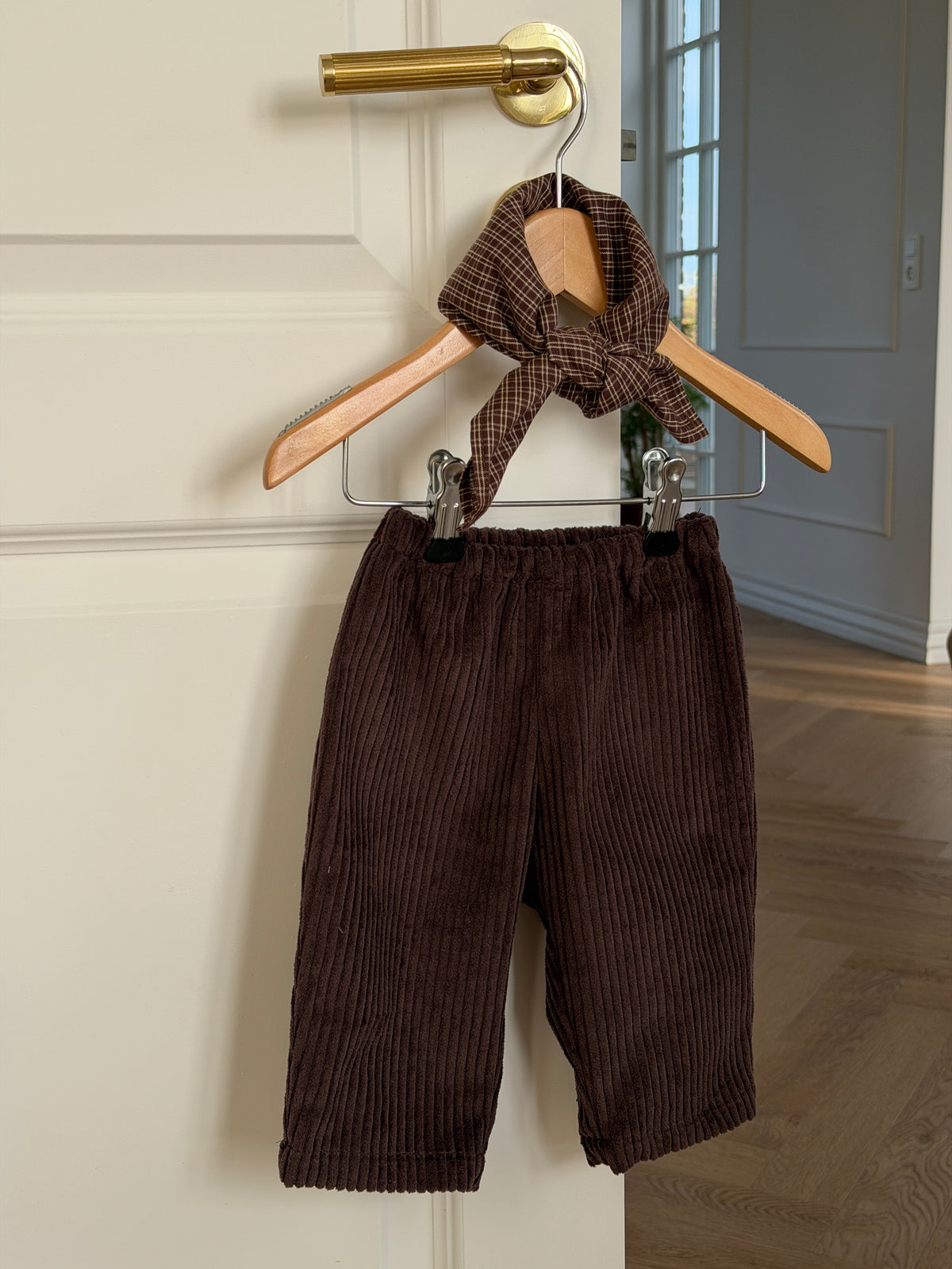 Brown velvet trousers and a brown checked scarf on a hanger on a white door